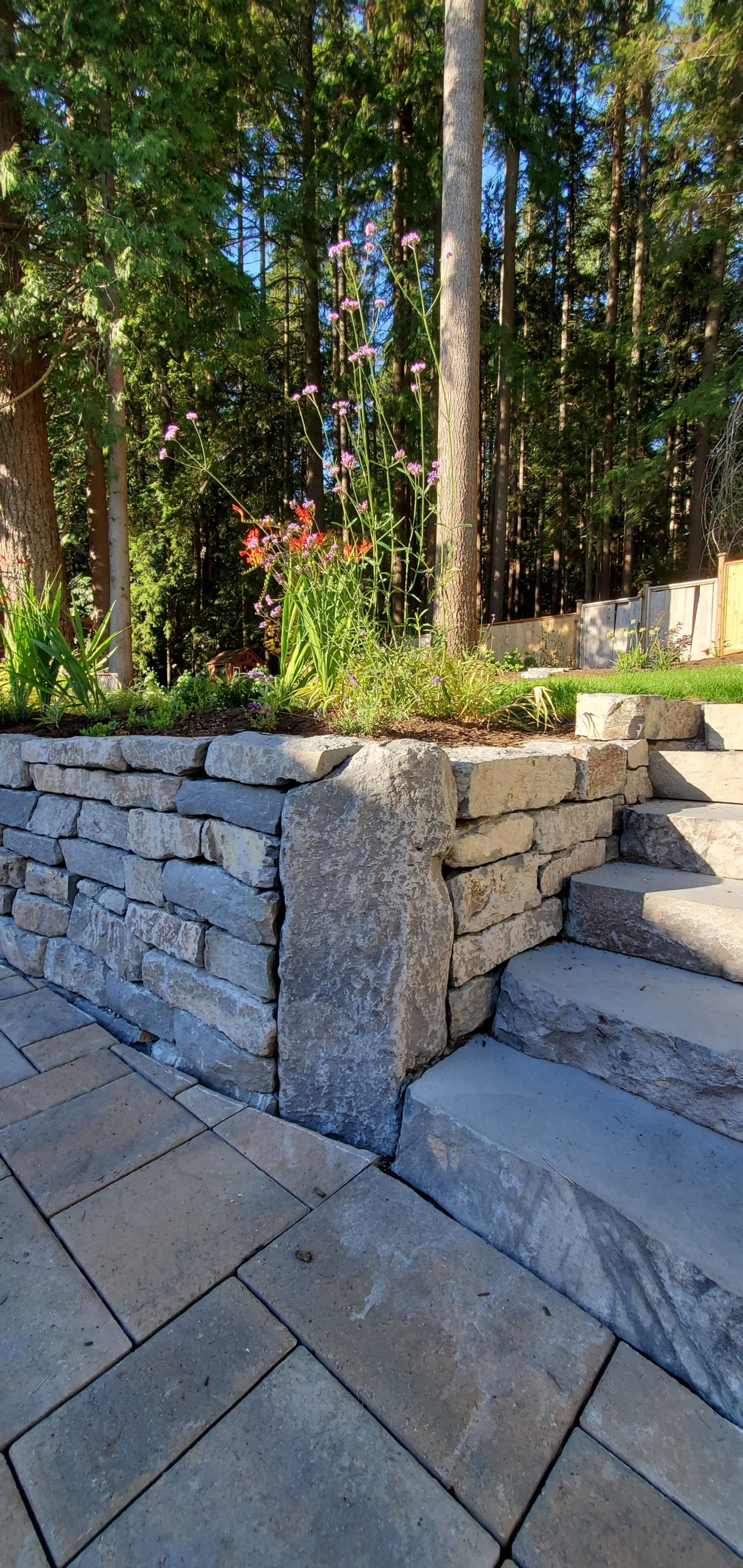 Basalt Stone Dry stack retaining wall with flowers and steps, surrounded by trees.