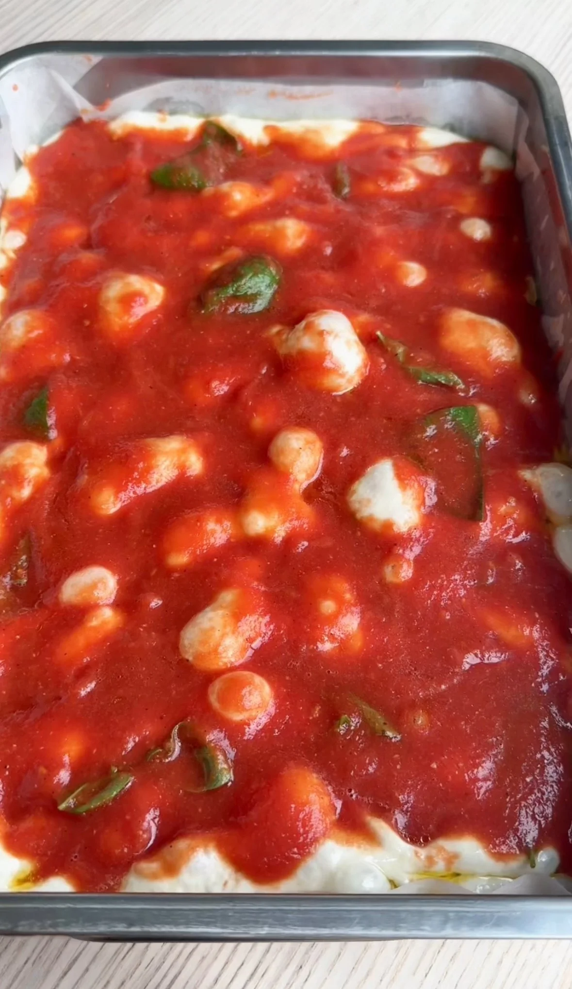 A baked dish with melted cheese, tomato sauce, and green herbs in a rectangular metal baking pan.