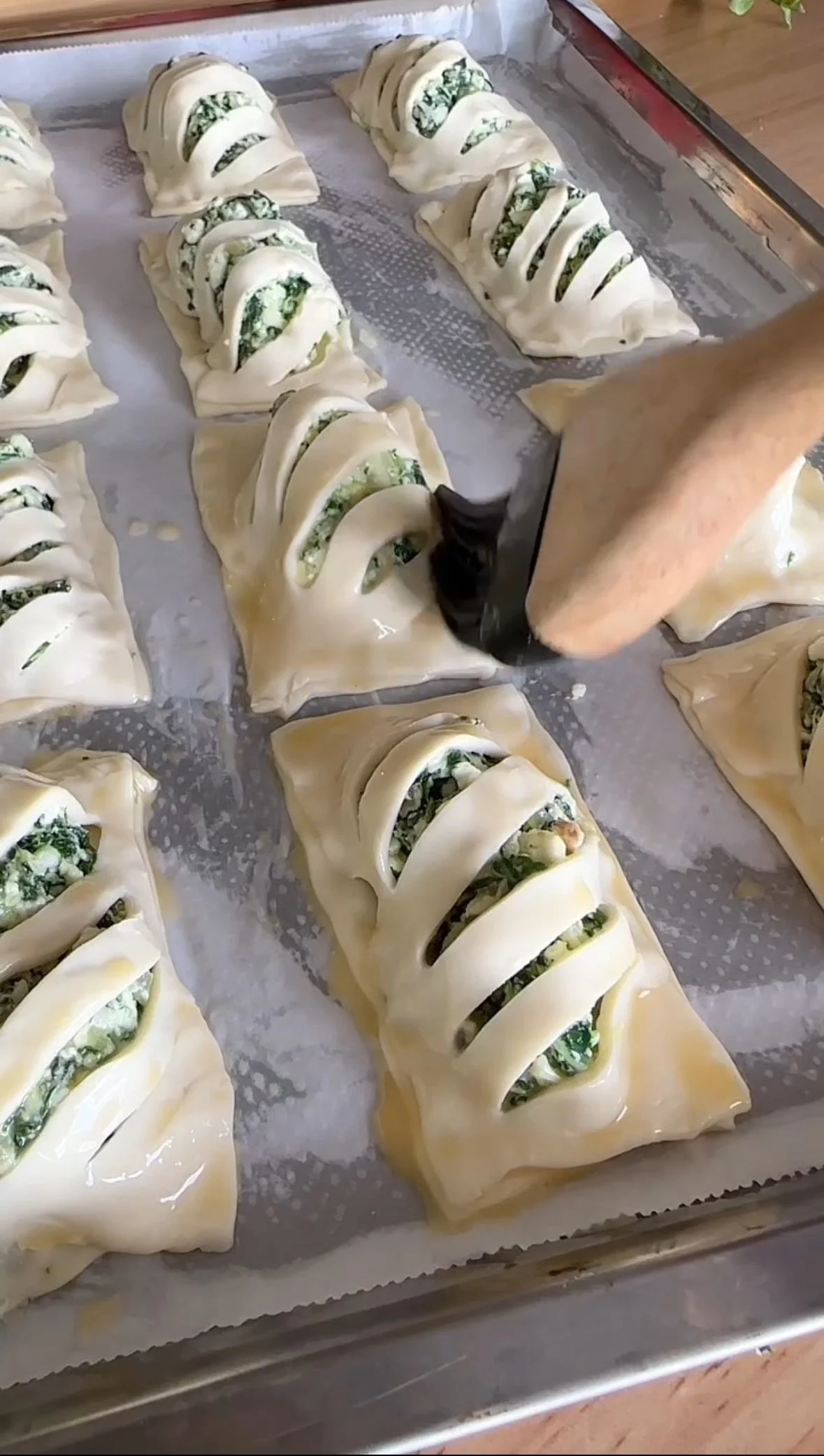 Person assembling spinach and cheese stuffed puff pastry pastries with slits on top on a baking sheet lined with parchment paper.