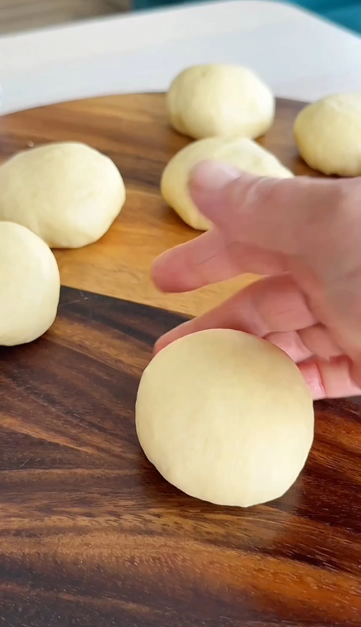 Multiple peeled potatoes on a wooden cutting board, with a hand reaching to pick up one.