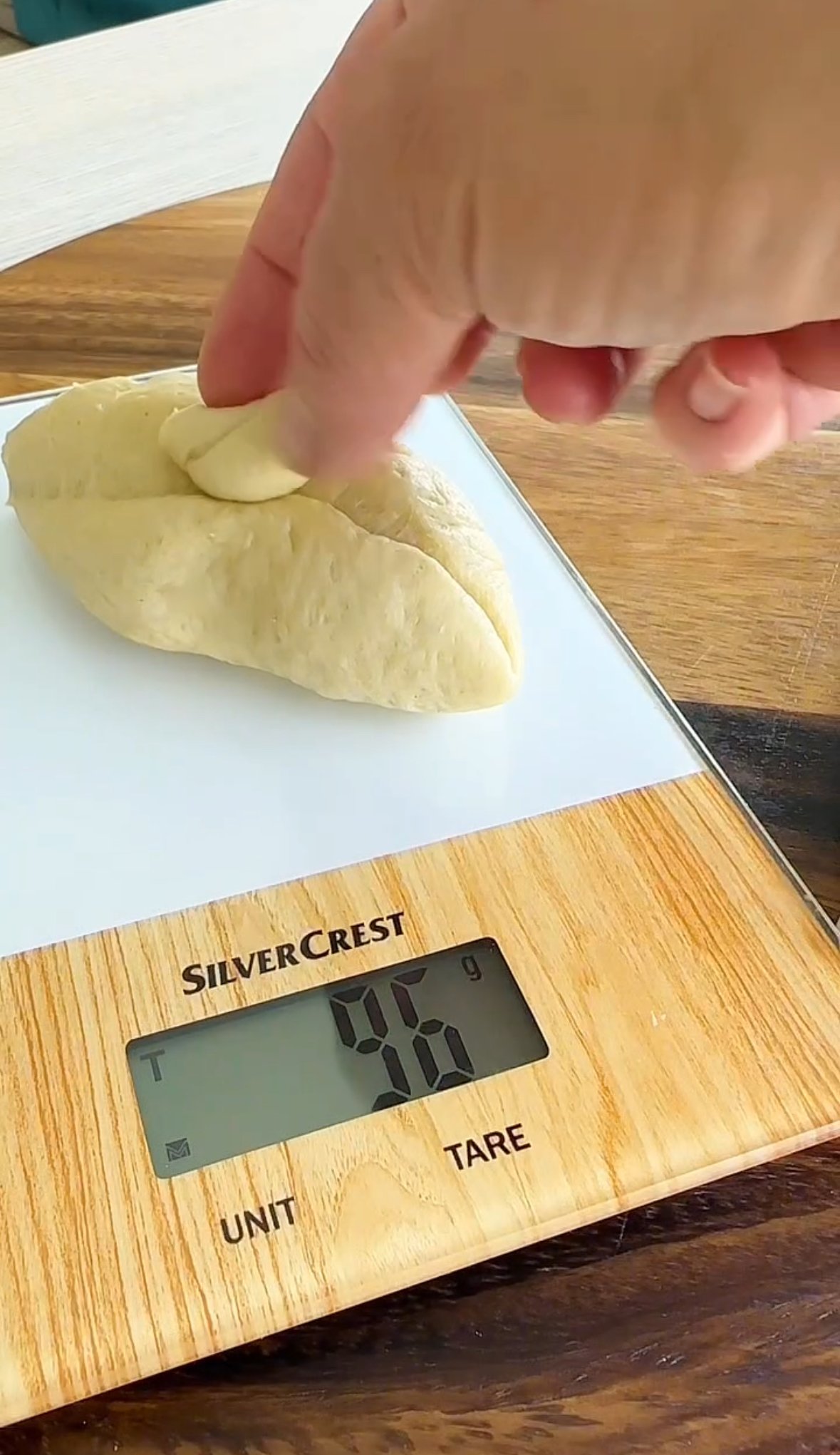 A person is sprinkling salt onto a folded piece of dough on a digital kitchen scale that reads 56 grams.