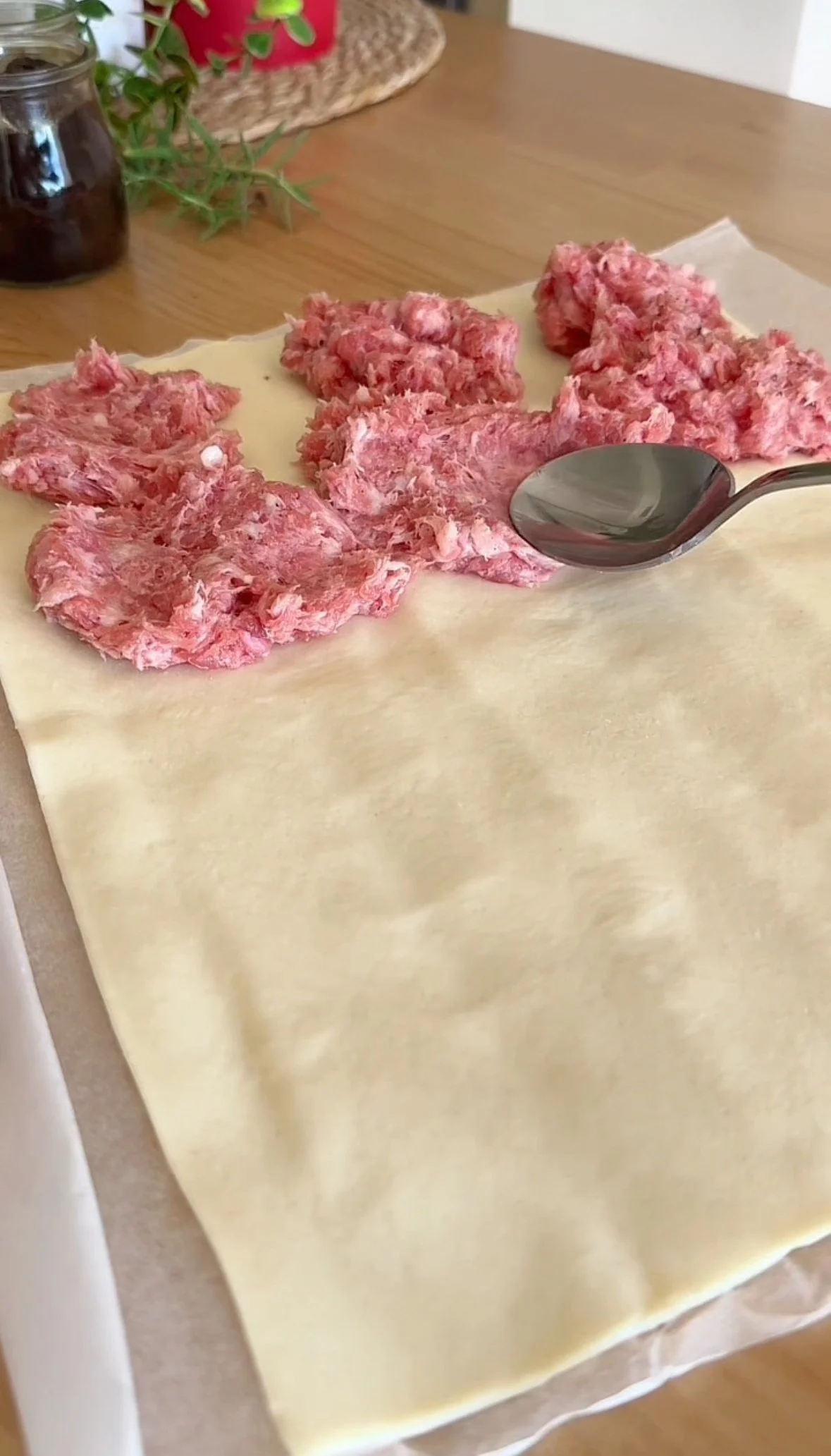 Raw ground meat on a sheet of pastry dough with a spoon on top, ready to be wrapped.