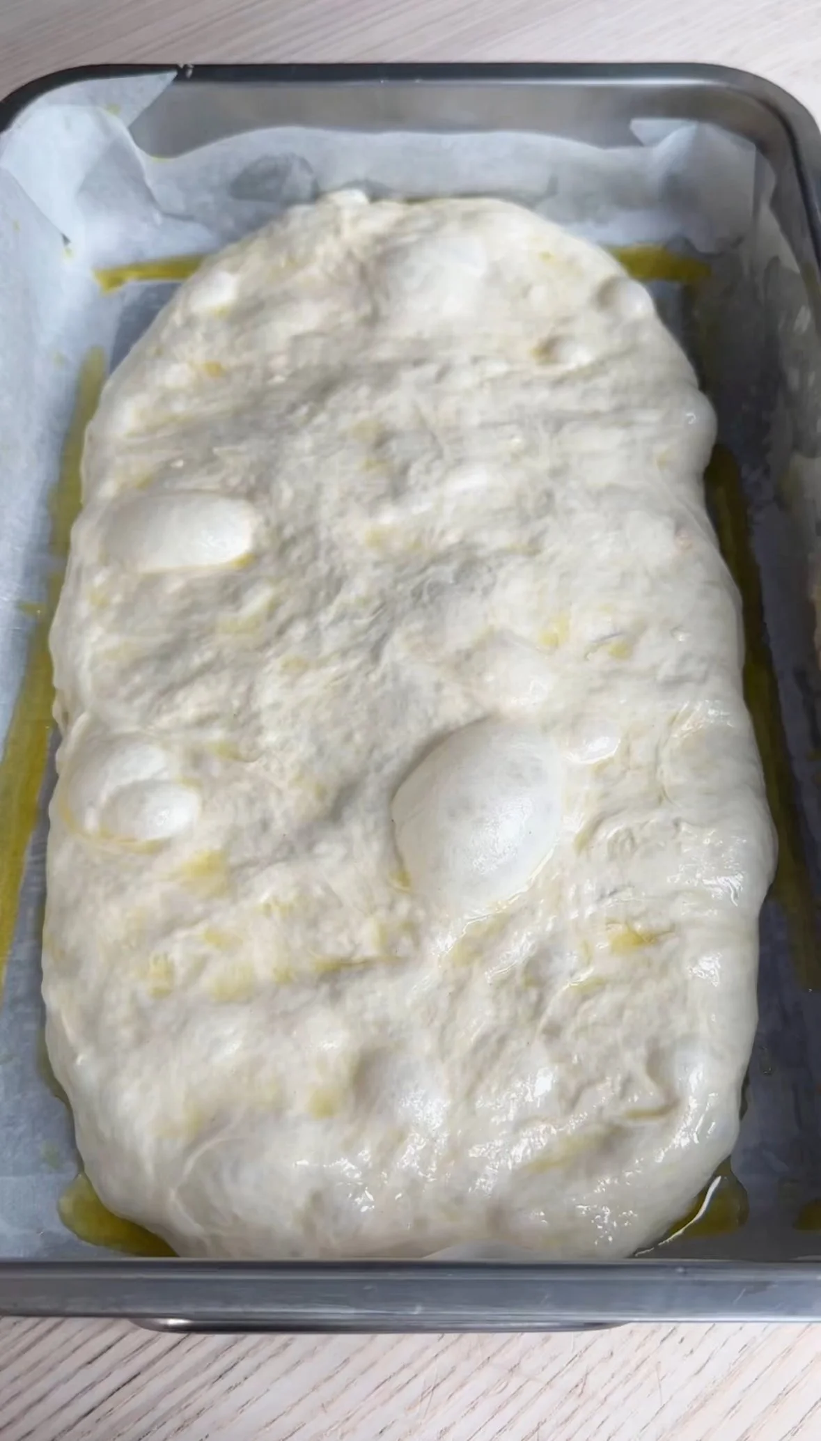 Dough rising in a baking pan lined with parchment paper.