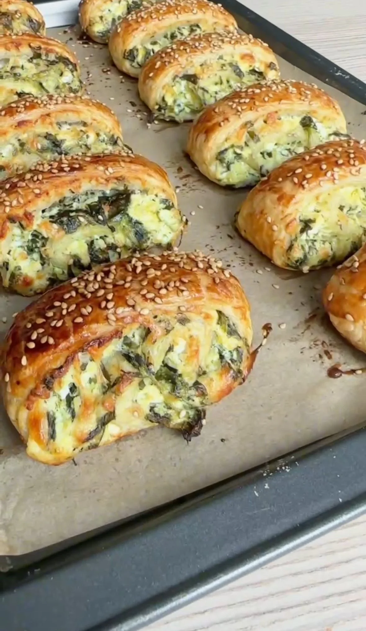 Baked spinach and cheese pastries on a baking sheet sprinkled with sesame seeds.