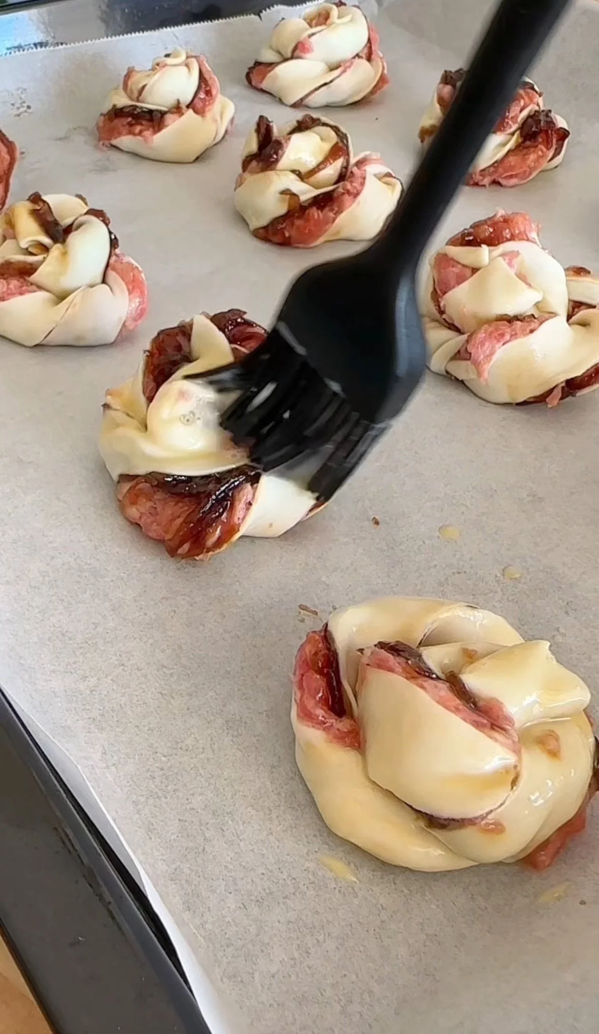 Uncooked ham and cheese stuffed pastry knots on a baking sheet.
