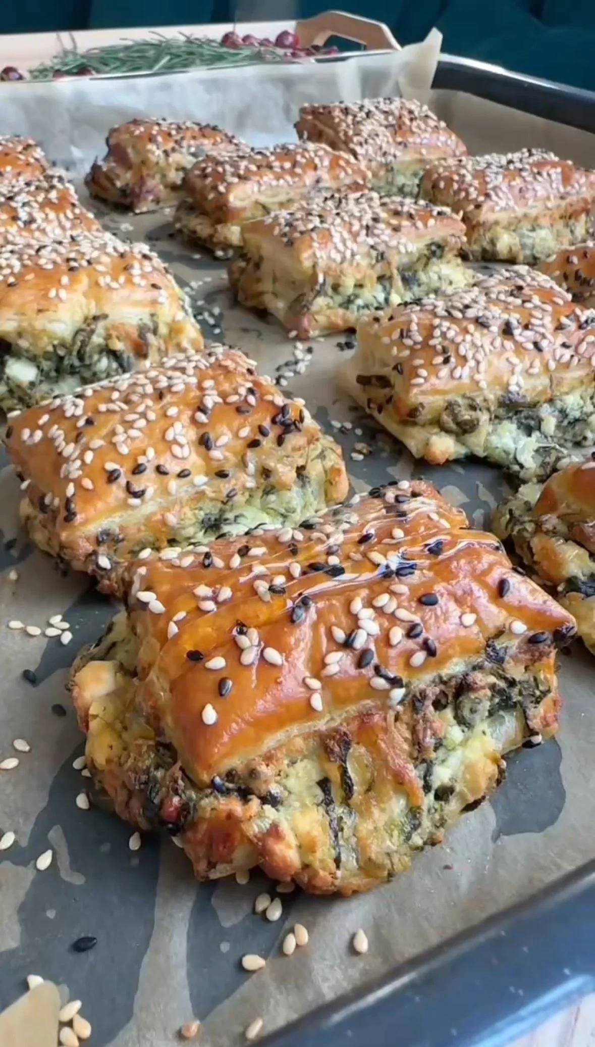 Baked savory pastries topped with sesame and black sesame seeds, on a baking sheet lined with parchment paper.