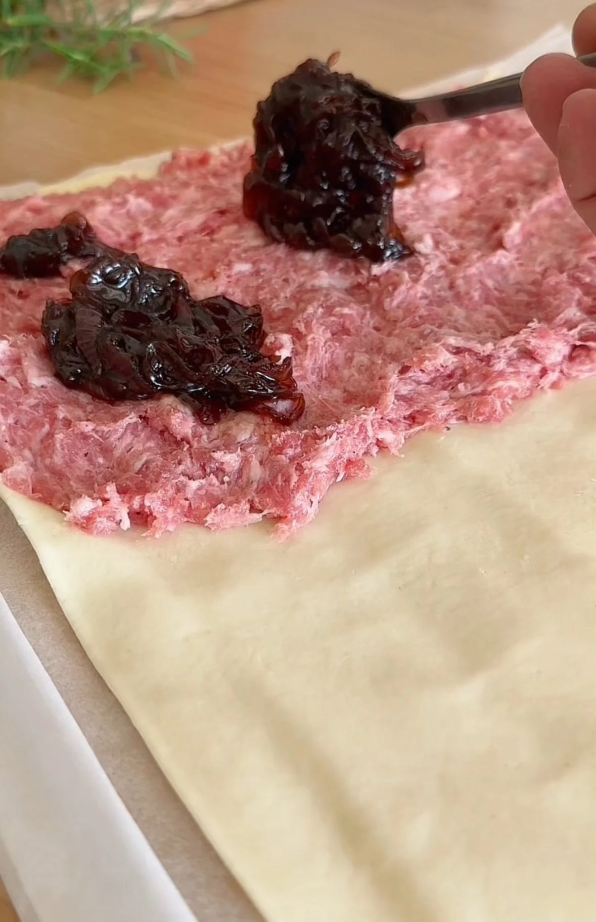Unrolled pastry with a layer of ground meat and dollops of fruit jam, possibly preparing a strudel.