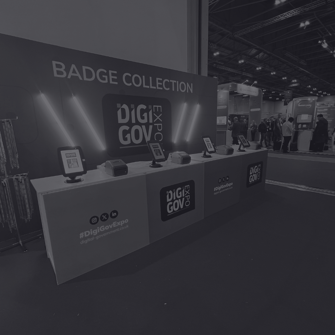 Crowd of people inside a large, historic event hall with high arched windows, a large screen on the wall, and some overhead lighting equipment.