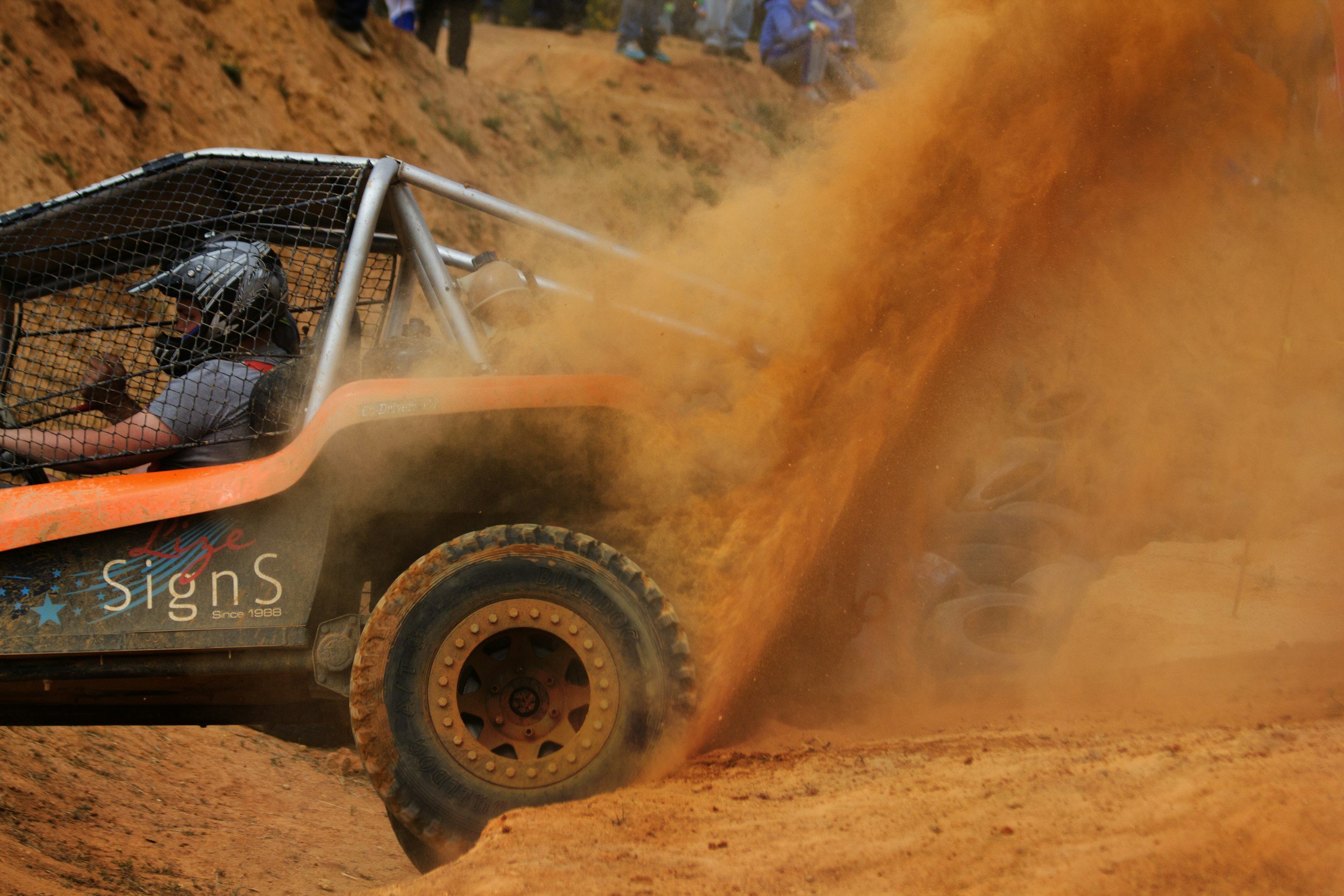 A person in a helmet driving an off-road vehicle kicks up dust on a dirt track.