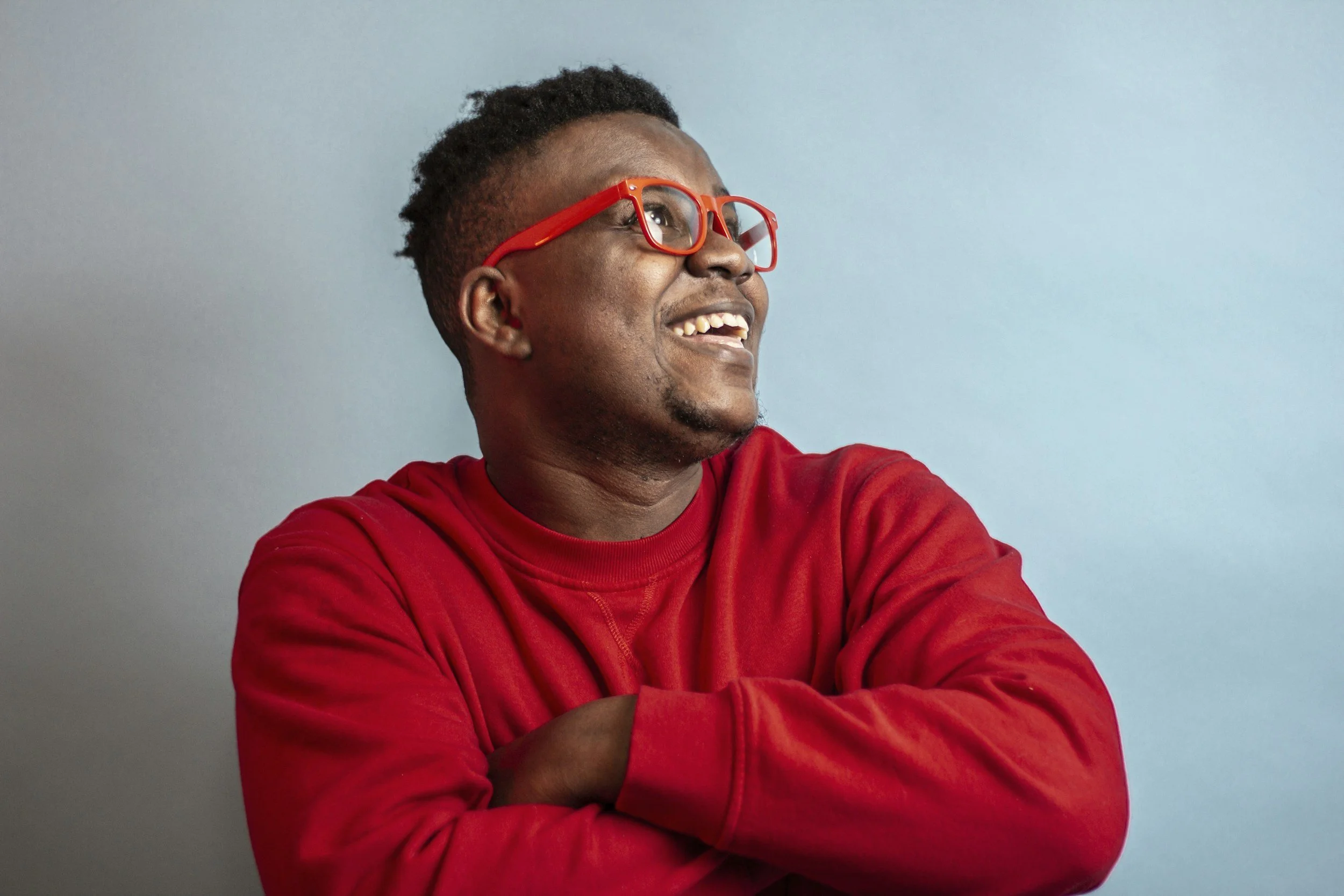 A young man with glasses and a red sweatshirt smiling and looking to his right against a blue background.