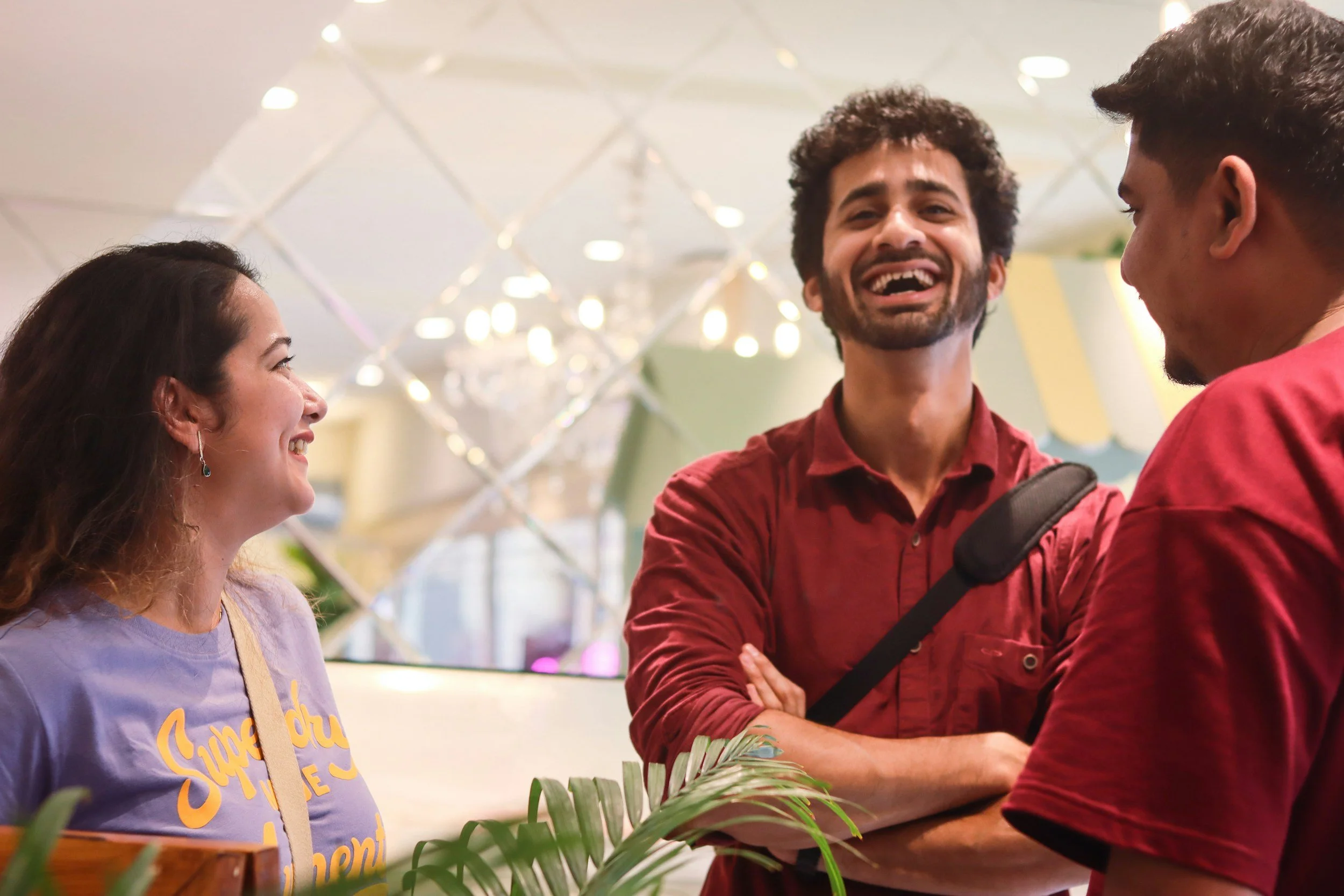 Three people chatting and smiling in an indoor setting with decorative lighting and greenery.