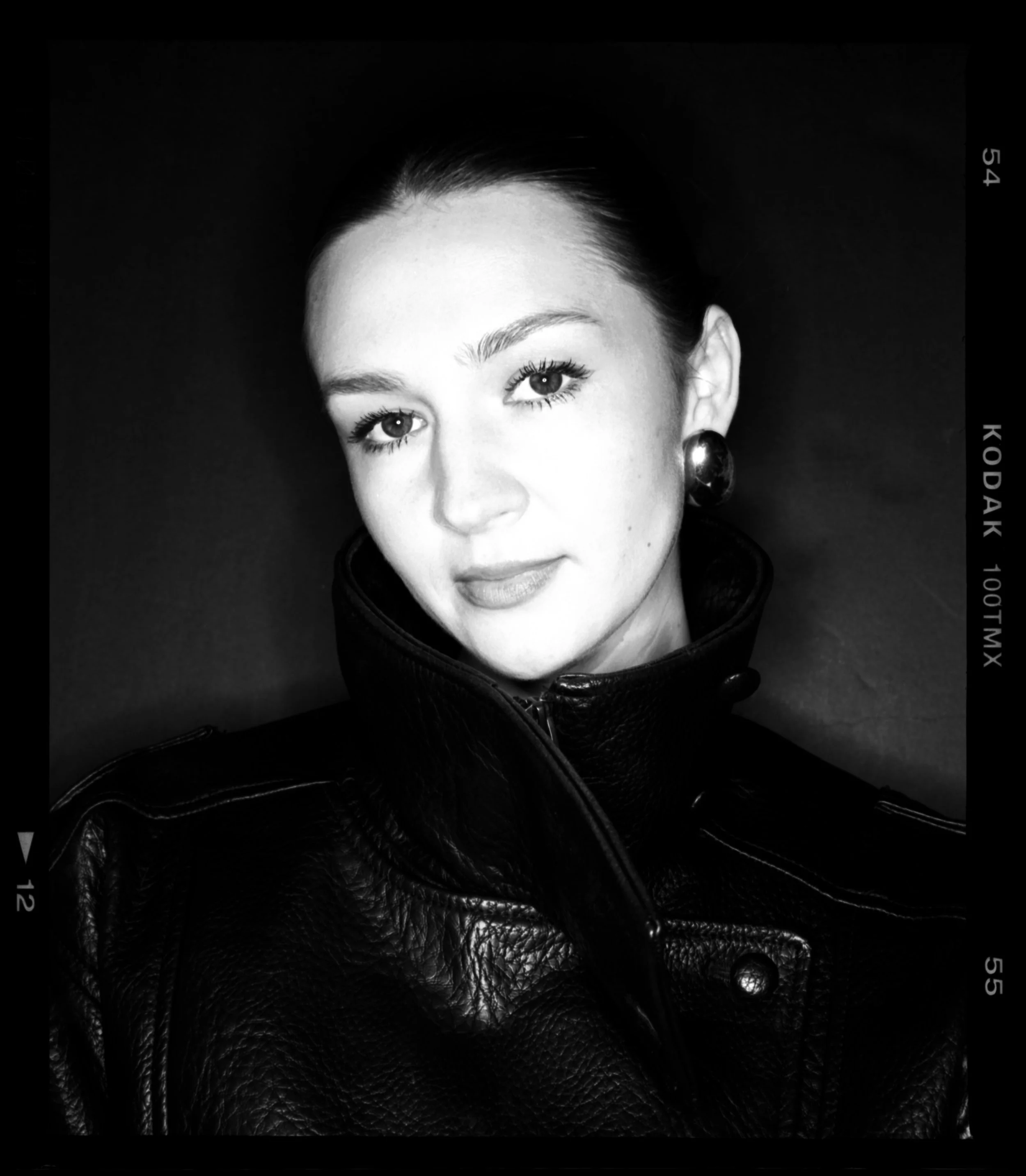 Black and white portrait of a woman wearing a leather jacket and large earrings, looking at the camera with a slight smile.