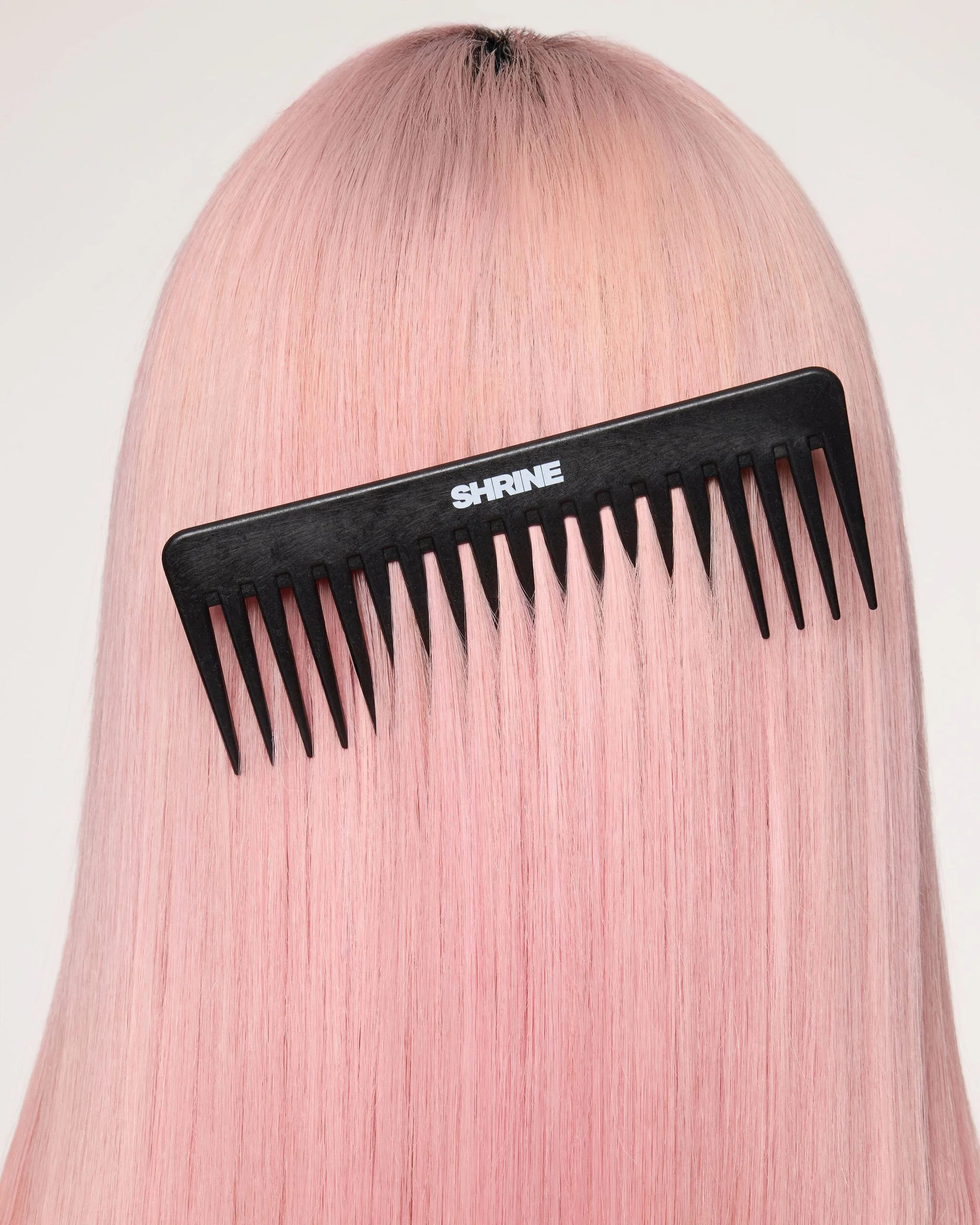Close-up of pink hair with a black wide-tooth comb labeled 'SHRINE' running through it.