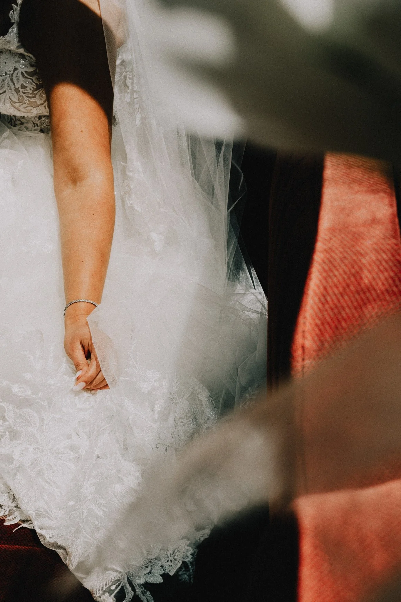 Close-up van een arm met trouwring en zichtbaar trouwkleed, gefotografeerd in de zonlicht in de trouwbus. Analoge en digitale huwelijksfotografie in België.