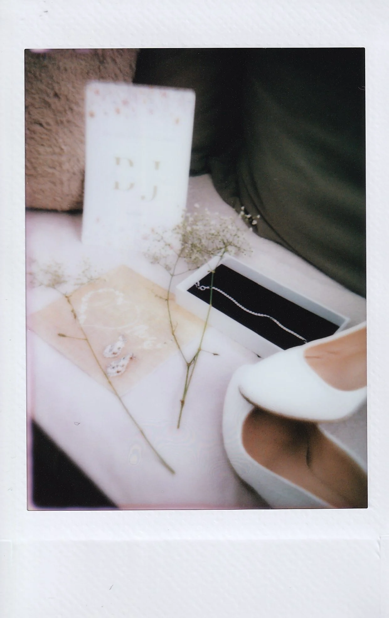 Collection of decorative items including a white electrical outlet, dried flowers, a rectangular jewelry box with a necklace, a pair of earrings, a white high-heeled shoe, and a black bag.