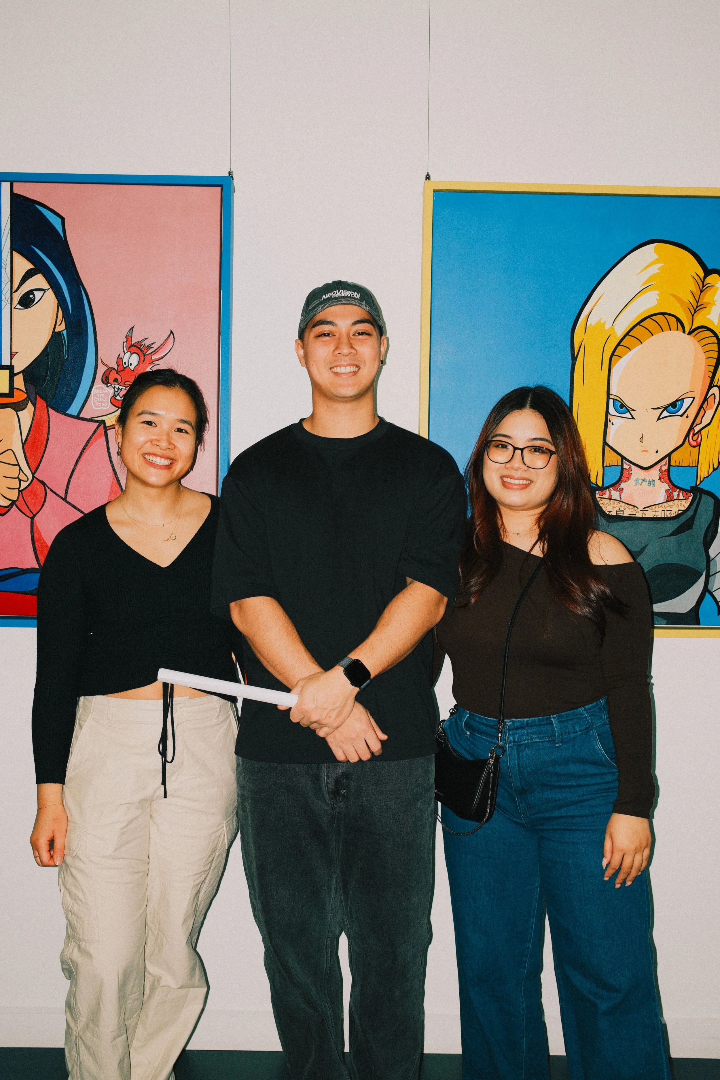 Three friends standing in front of colorful cartoon paintings at an art gallery.
