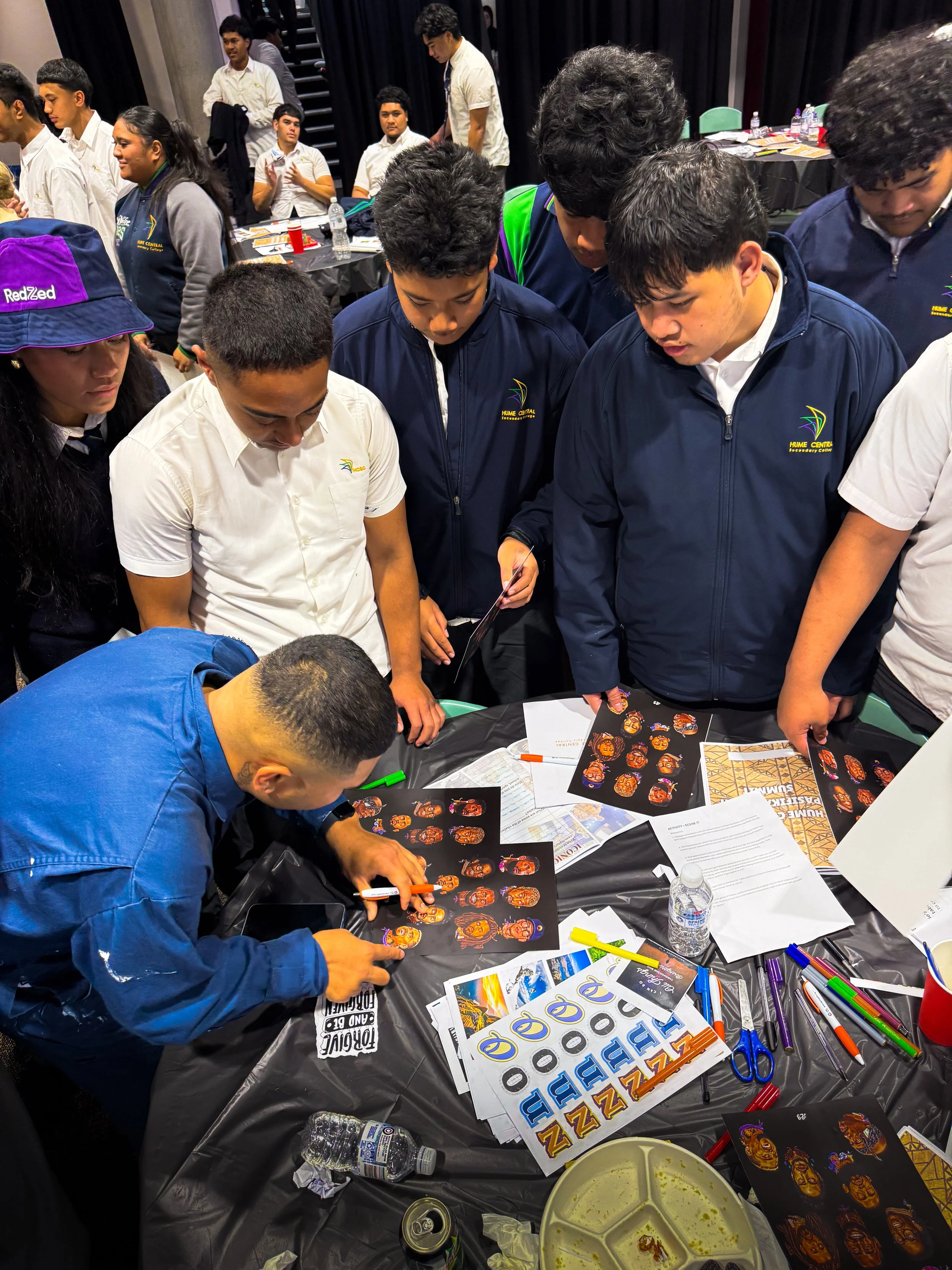Group of students around a table looking at stickers and printed materials at an indoor event.