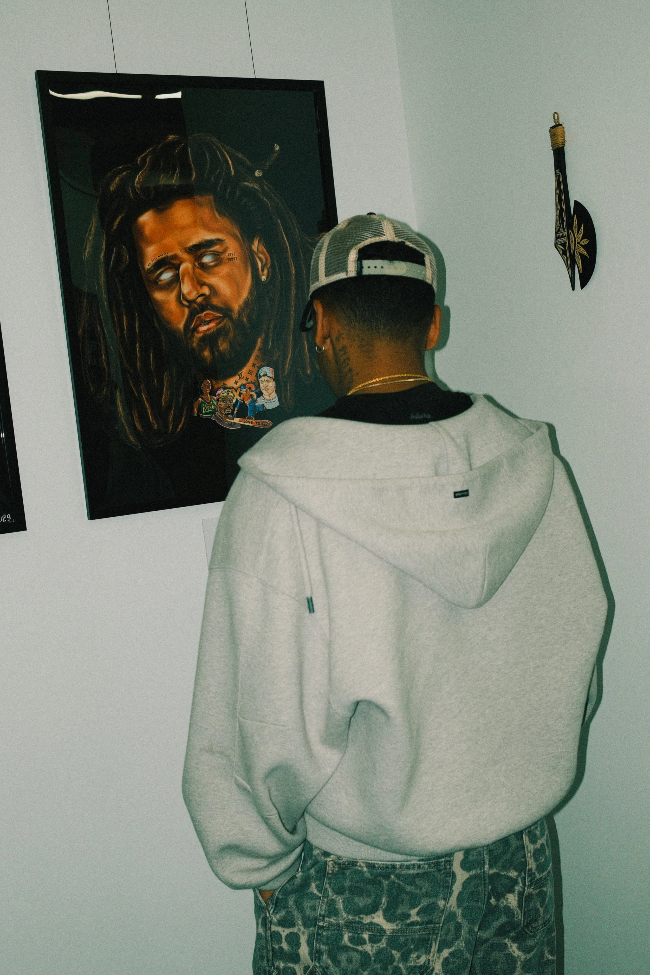 A man with a cap and hoodie looking at a portrait of Bob Marley on a gallery wall.