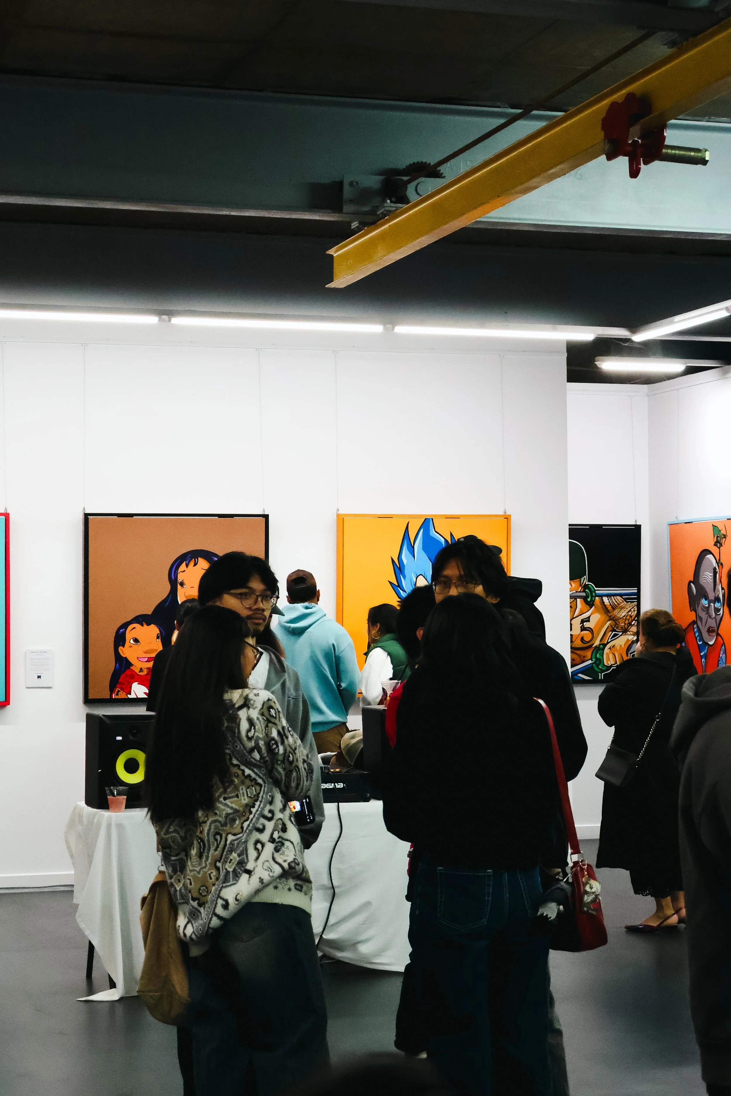 People attending an art exhibition with colorful paintings hanging on white walls.