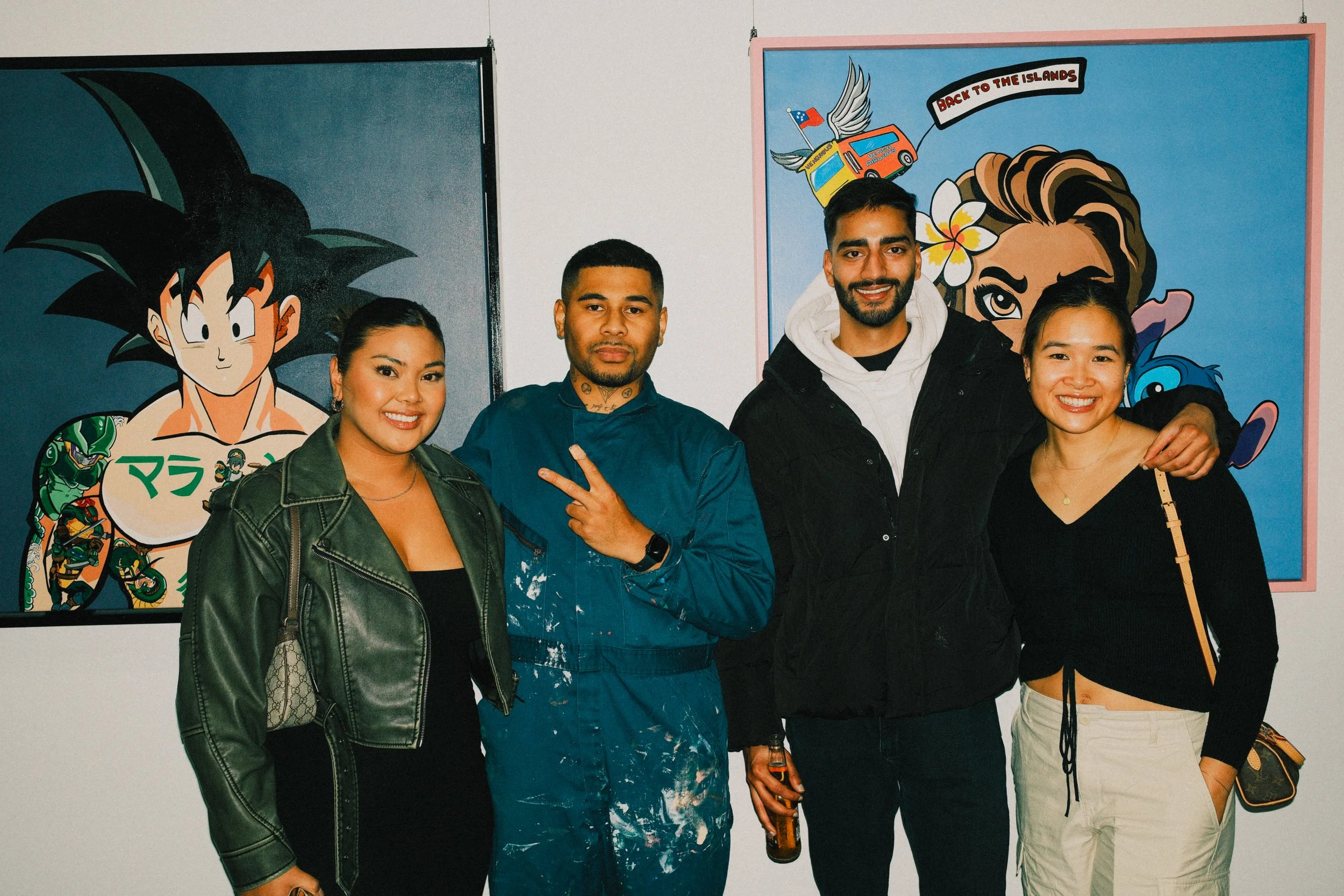 Four people standing in front of colorful paintings of anime characters, smiling and posing for a photo.