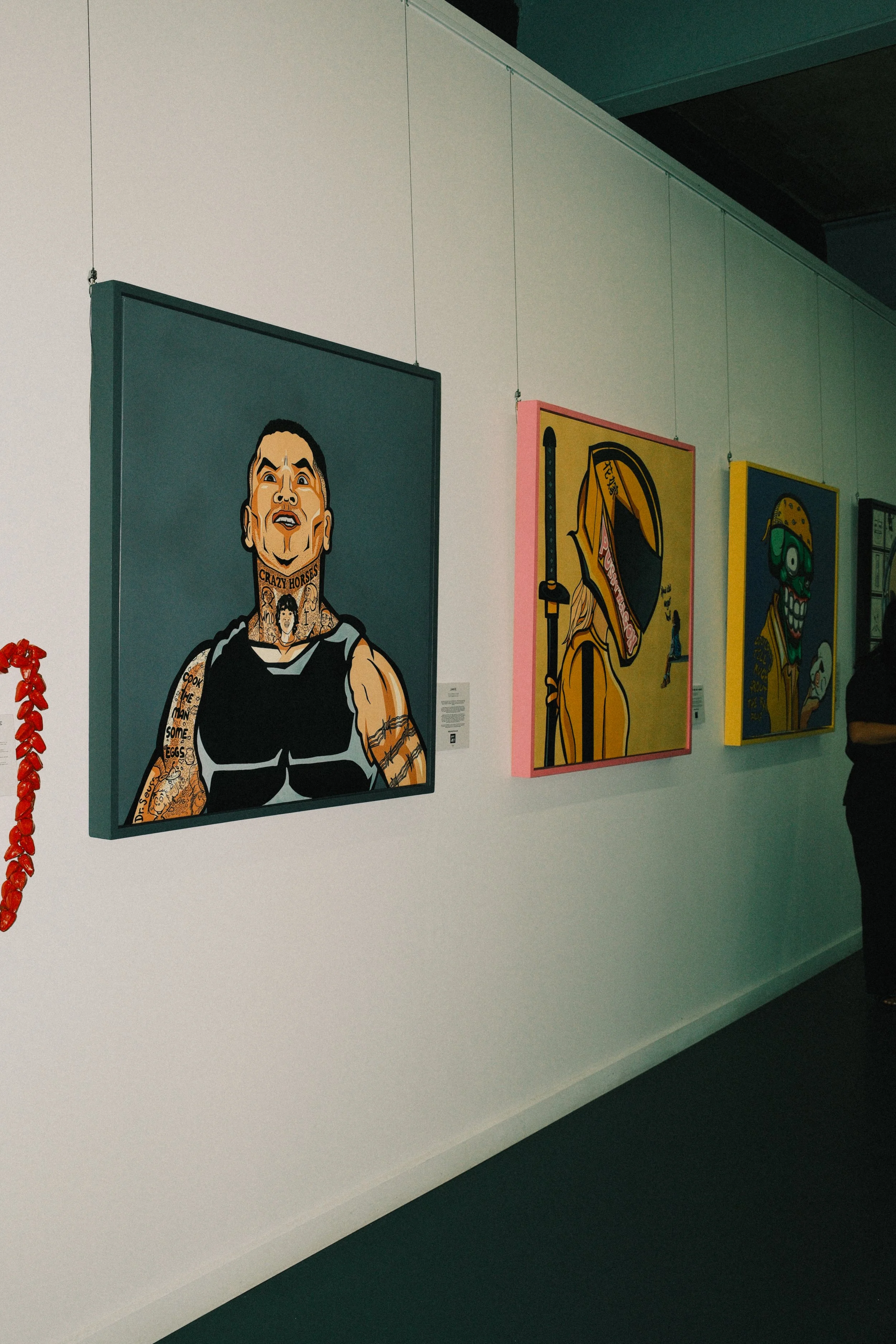 Colorful artwork on display at an art gallery, featuring pop art-style portraits of cartoonish and animated characters in bold colors.