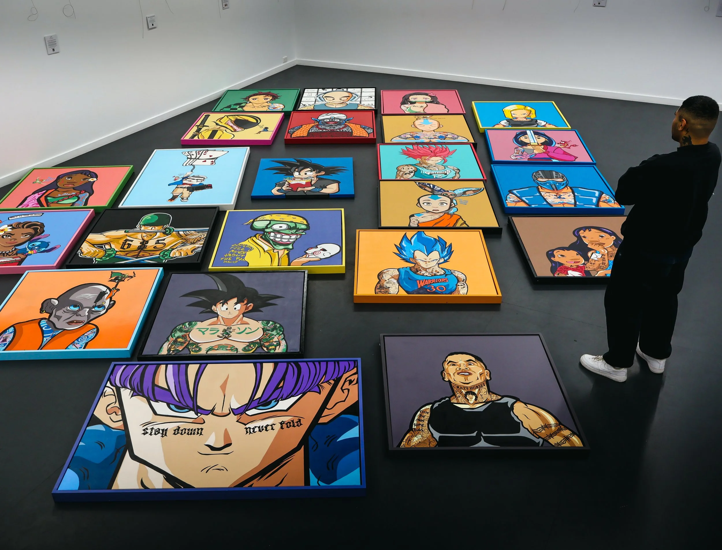 Colorful framed portraits of various animated characters are arranged on the floor in a gallery-like setting, with the artist Jeremy observing the artwork.