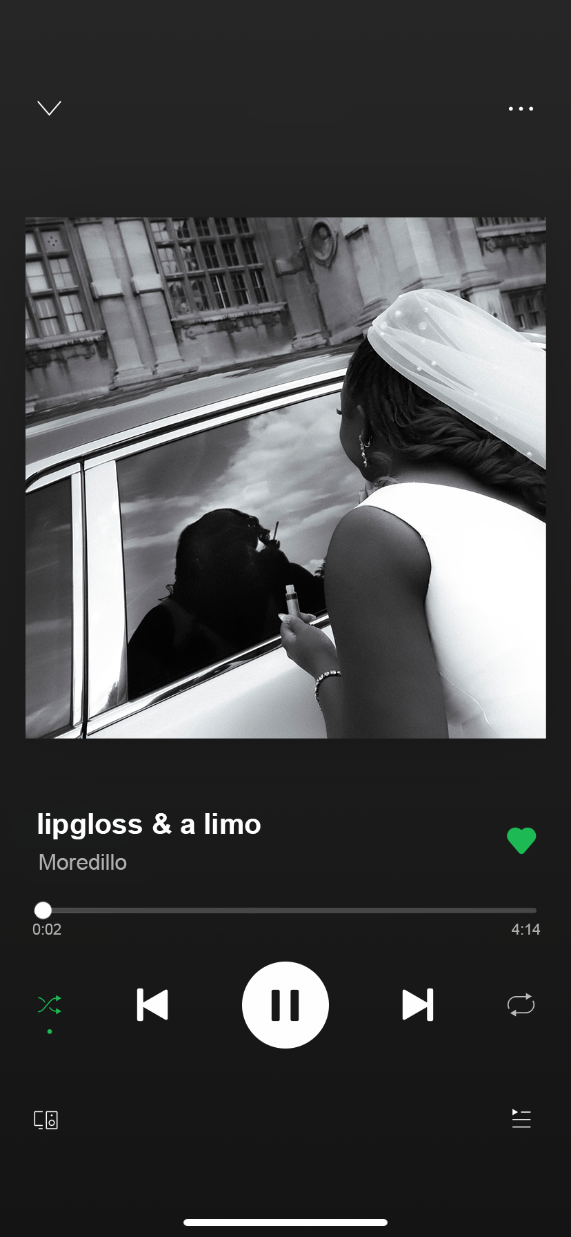 A woman in a wedding dress and veil leaning against a vintage car, holding an item in her hand, with a reflection of a man smoking in the car window, outside a historic building.