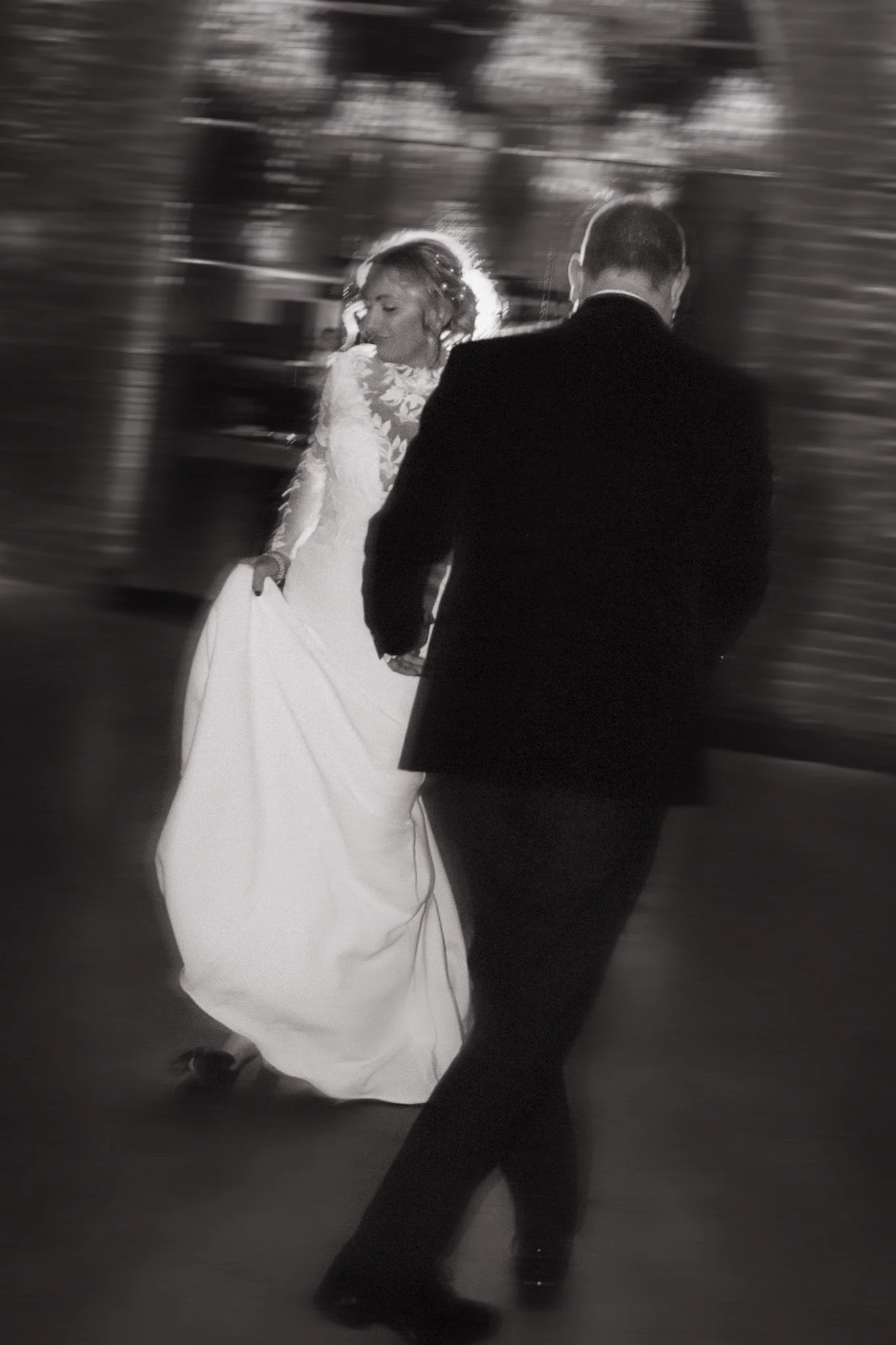 A bride in a wedding gown dancing with a groom dressed in a suit, captured in black and white with motion blur.