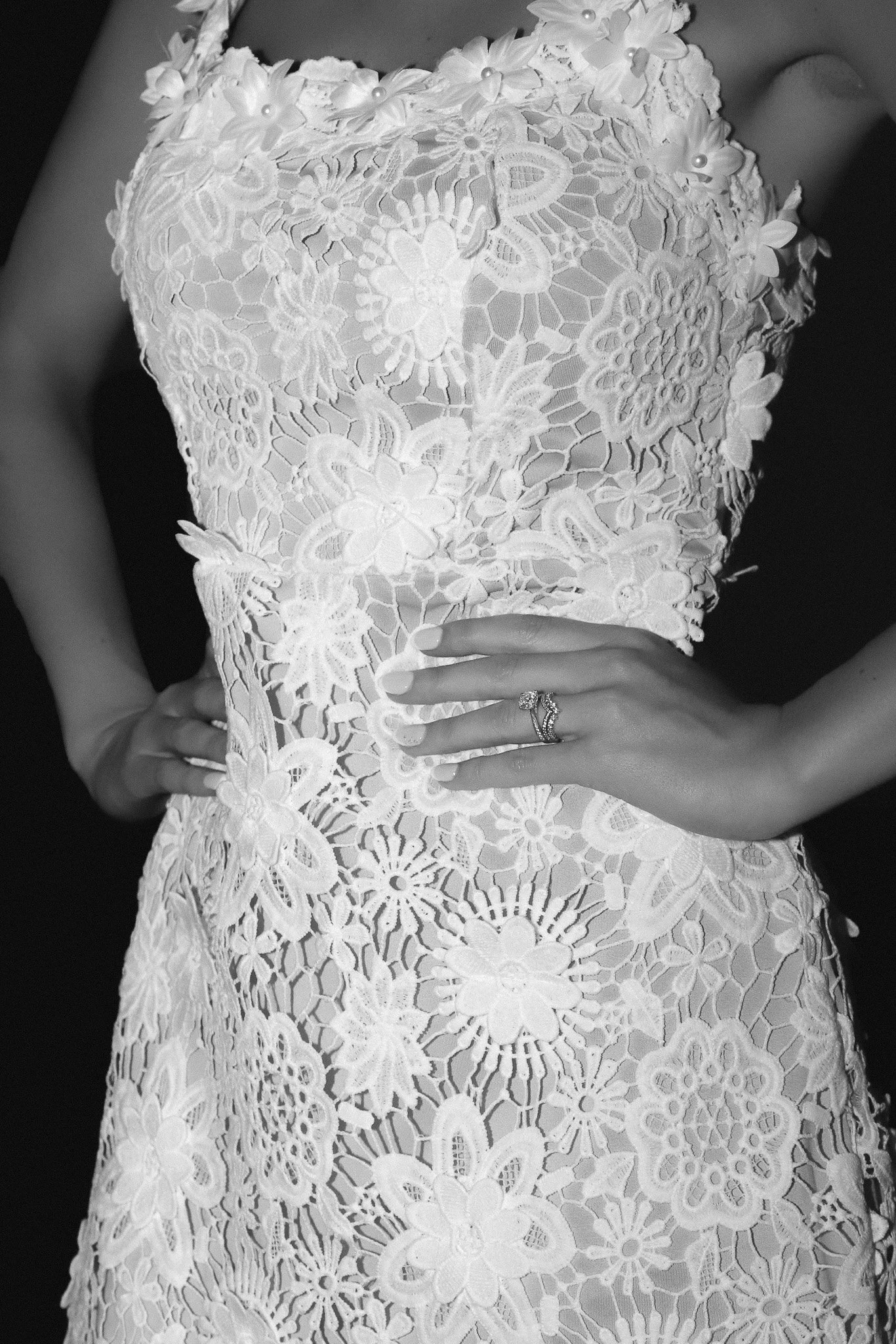 Close-up of a woman wearing a lace dress with floral embroidery, showing her hand on her waist with a ring.