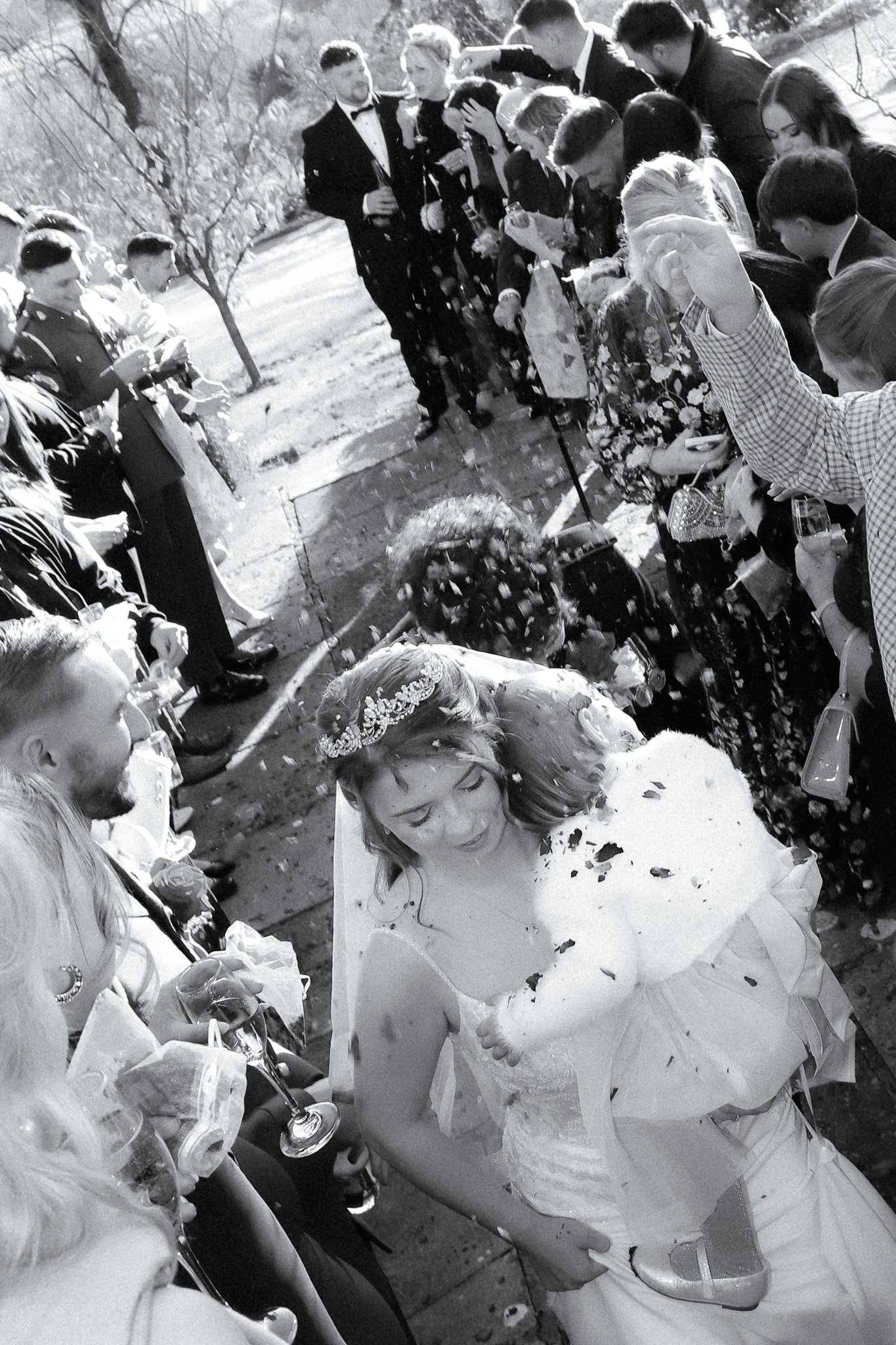 A bride holding a puppy during a celebration, surrounded by guests who are throwing confetti.