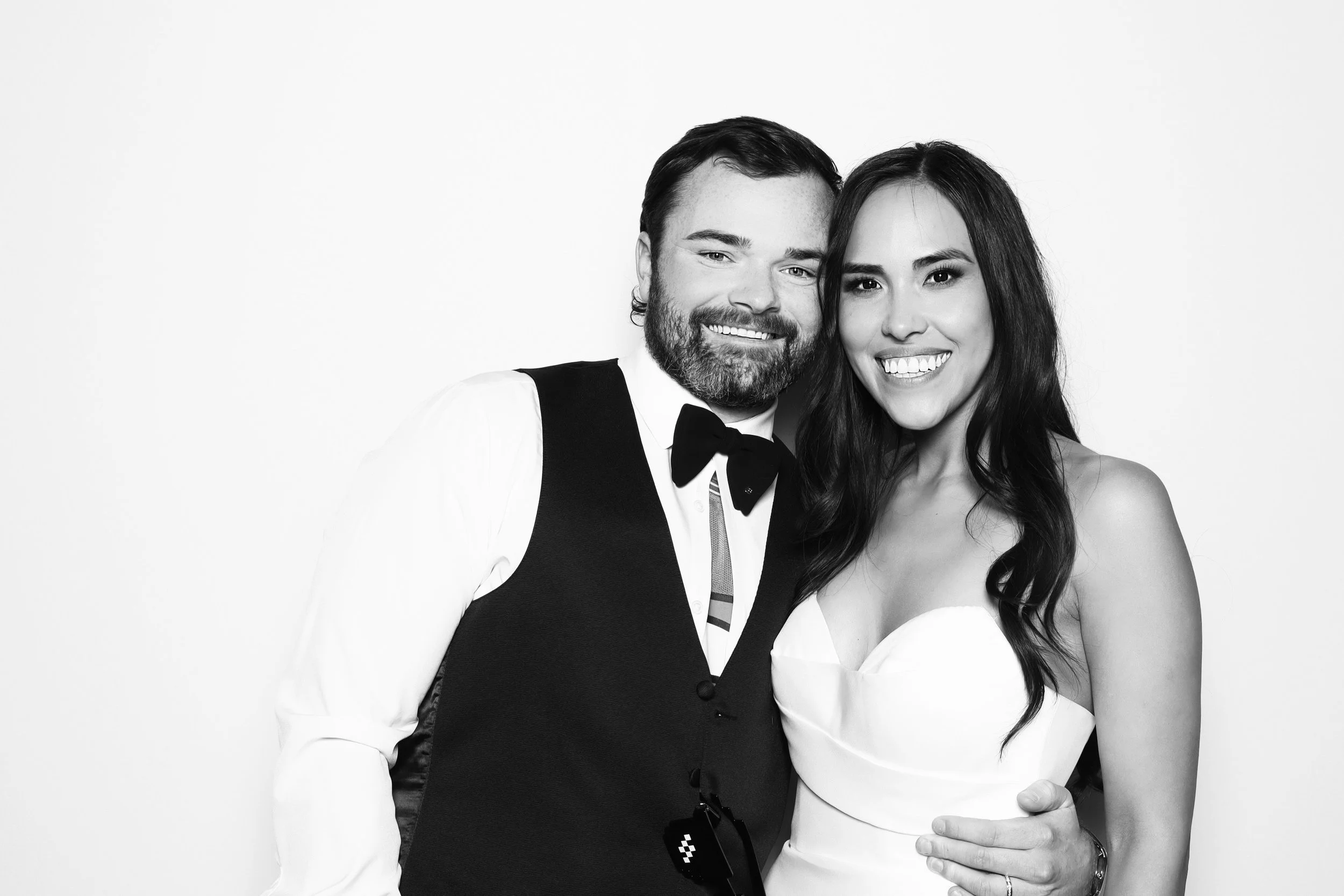 Black and white photo of a smiling man and woman in formal attire, embracing each other against a plain white background.