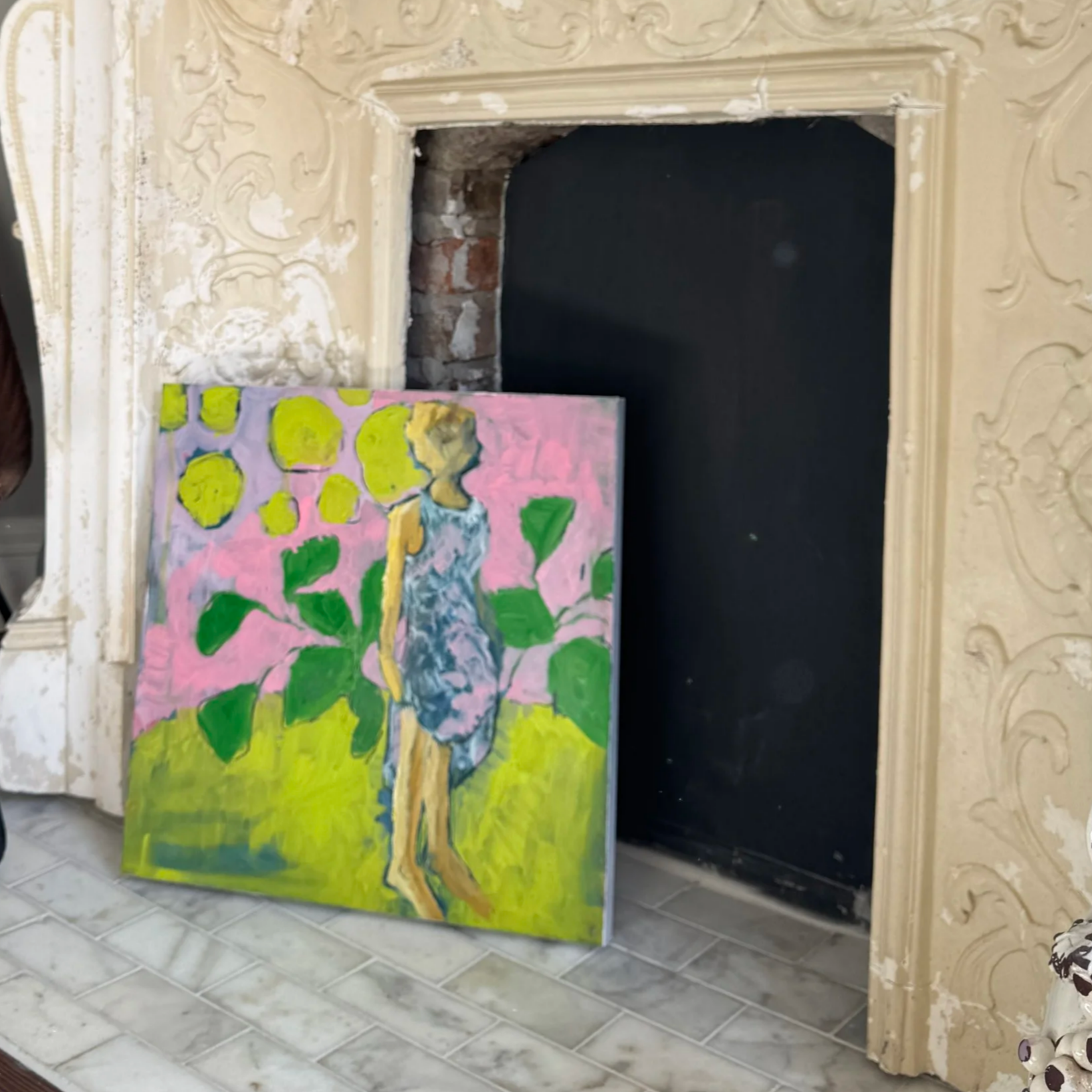 Colorful impressionist-style painting of a woman walking with a dog on a pink path, surrounded by green foliage, propped against a fireplace with ornate cream-colored trim.