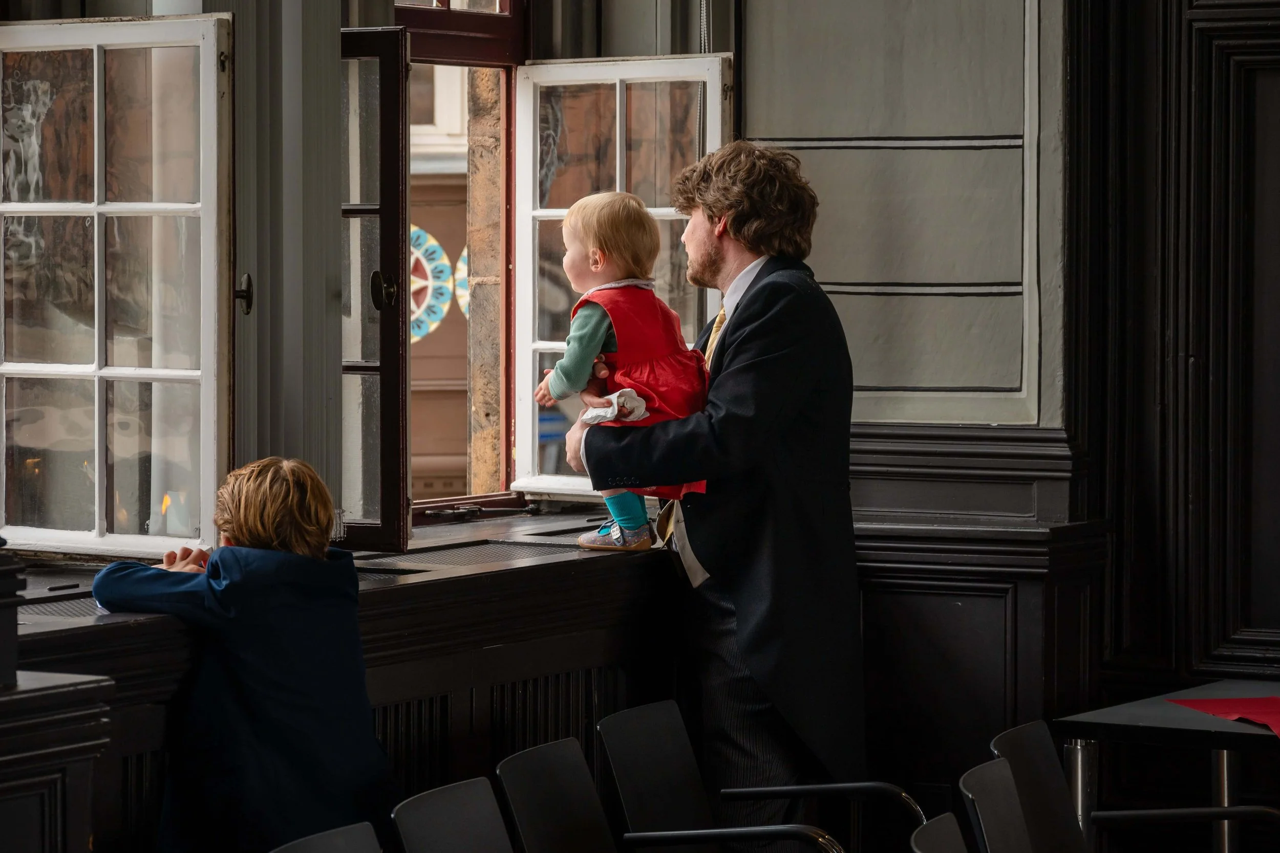 Ein Mann hält ein kleines Mädchen am Fenster, während ein Junge im Vordergrund nach draußen schaut. in Trauungssaal in Marburg