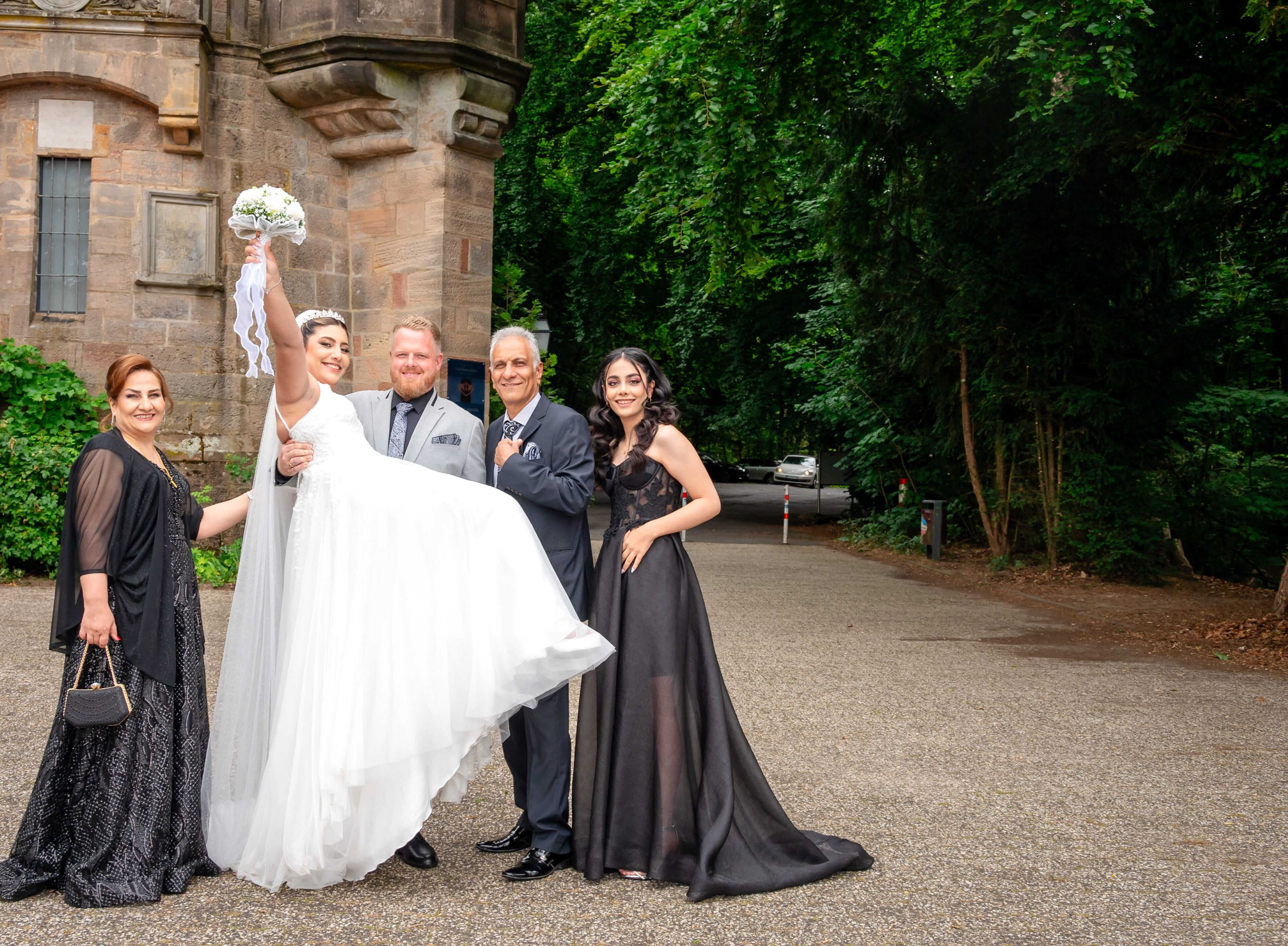 Hochzeitspaar in festlicher Kleidung mit drei weiteren Personen vor einer alten Kirche in Marburg