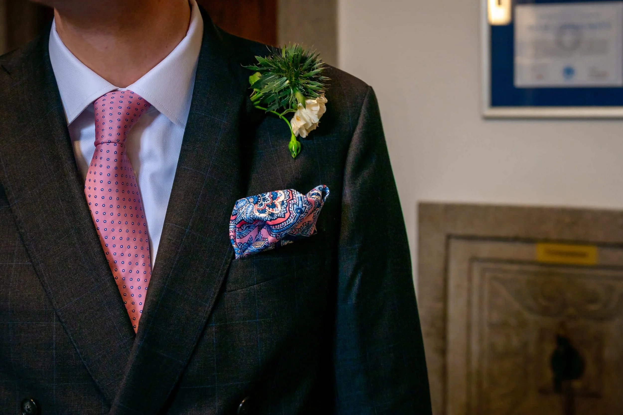 Mann in dunklem Anzug mit weißem Hemd, rosa Krawatte und farbigem Einstecktuch, trägt einen grünen Strauß aus Blumen an der Schulter. in Trauung in Marburg