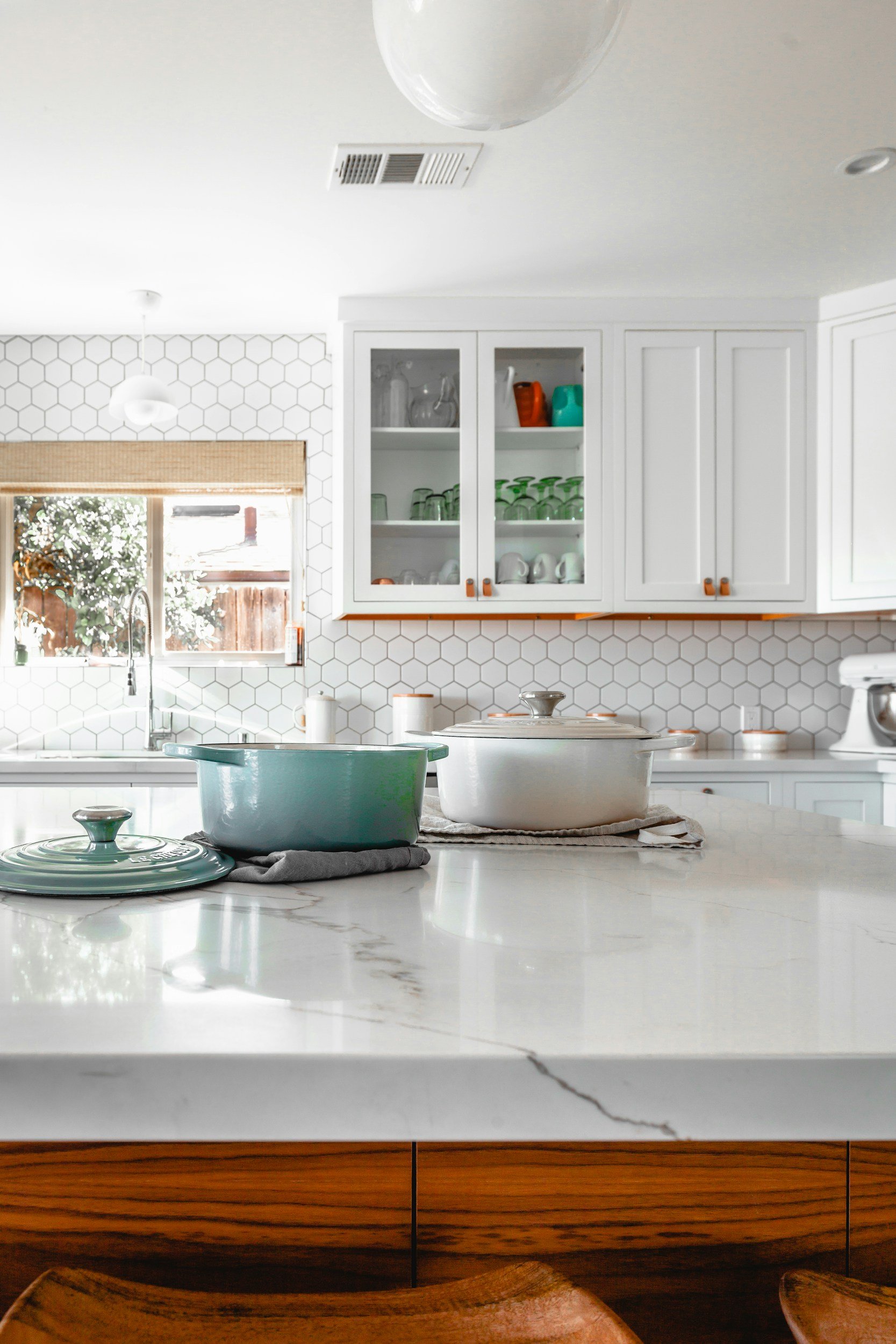 Modern kitchen with white hexagon tile backsplash, white cabinets with orange accents, and a marble countertop. Beautiful and professionally crafted stone coutertops.