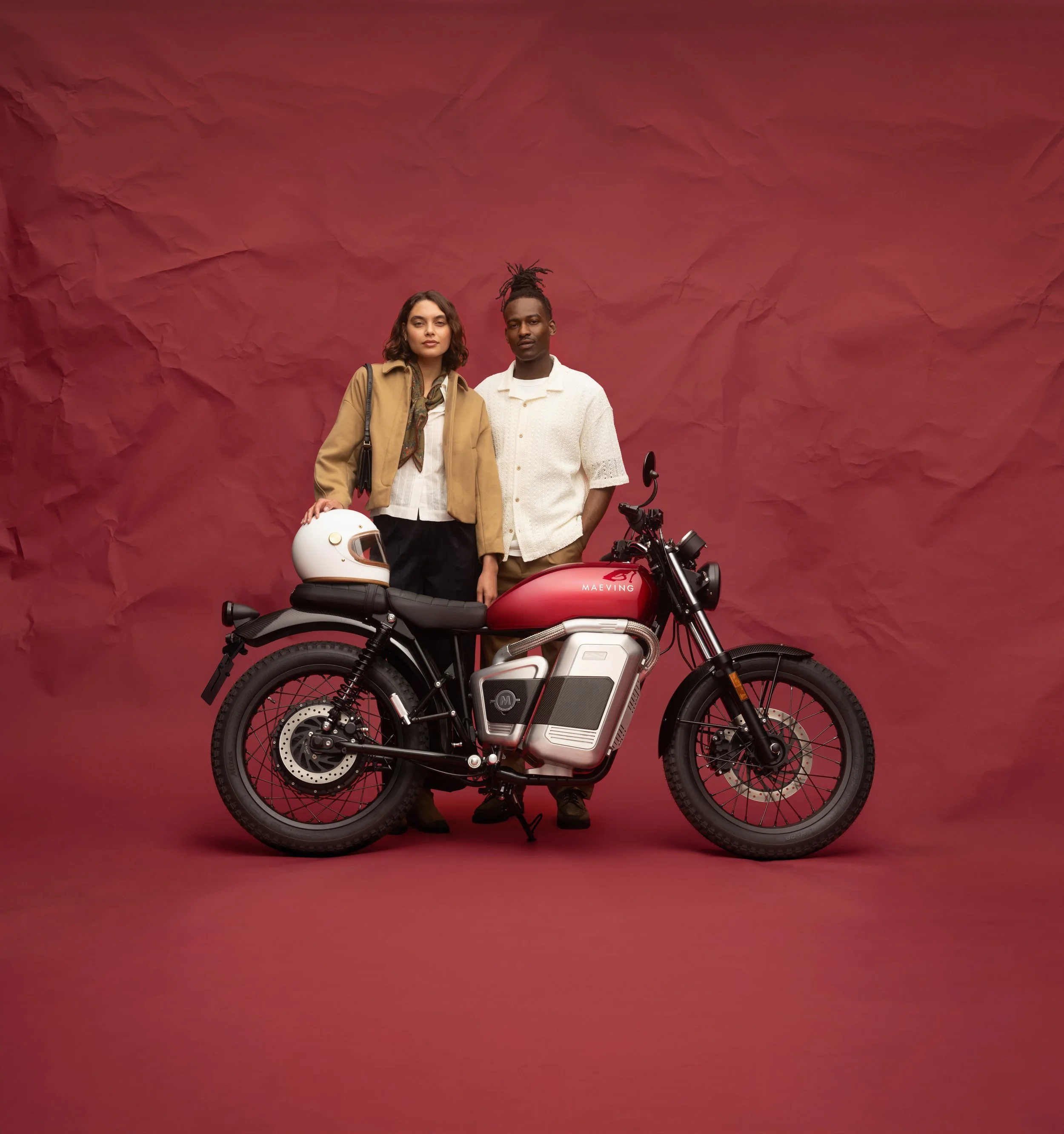 Deux personnes posent devant un fond de couleur rouge avec une moto électrique et un casque de moto.