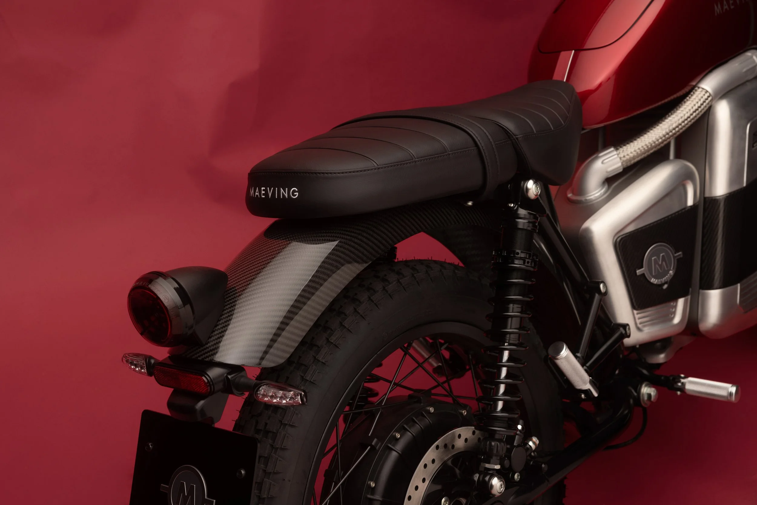 Une moto électrique rouge avec un siège en cuir noir et des composants en acier et fibre de carbone, contre un fond rouge.