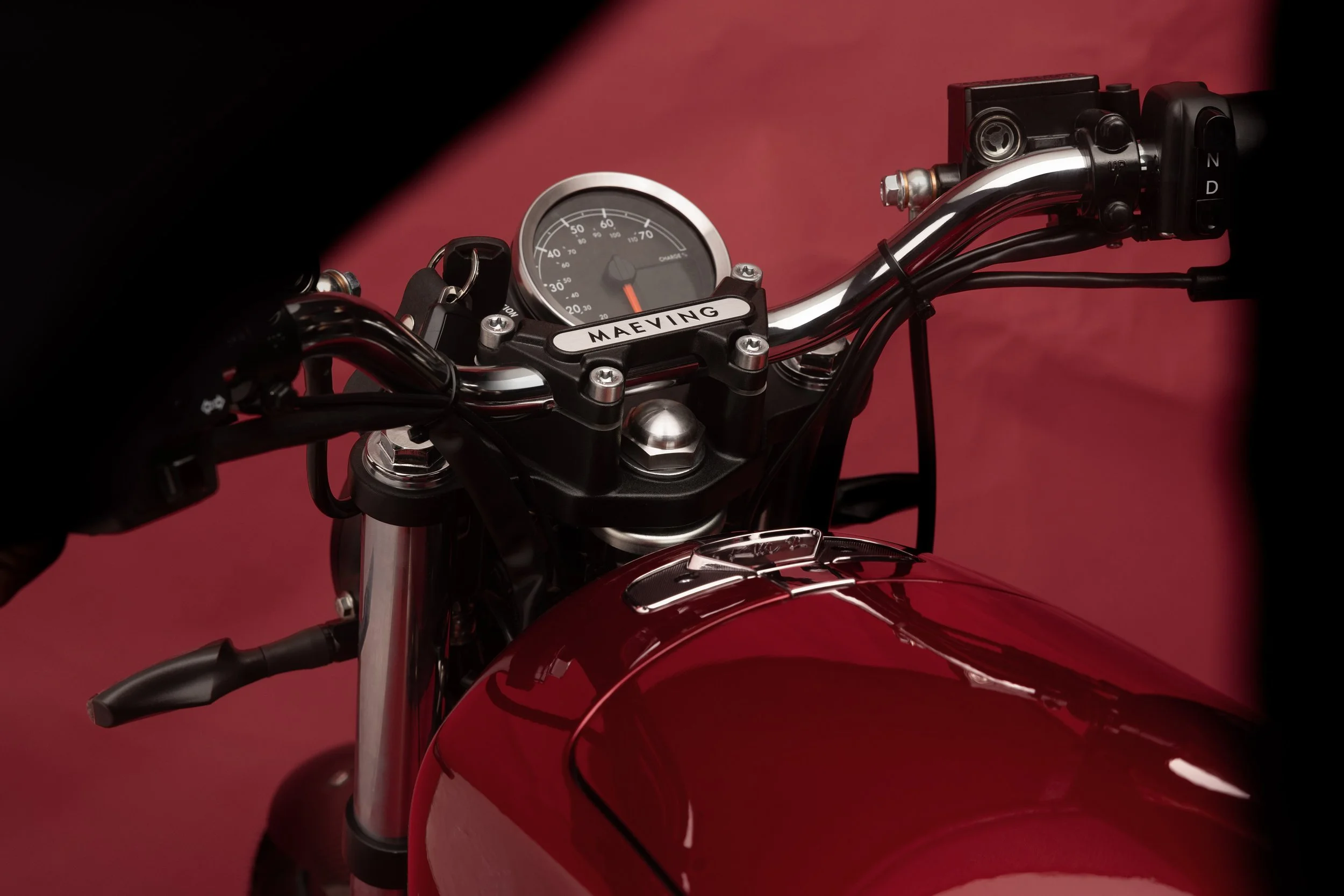 Instrument de moto électrique avec compteur de vitesse et guidon, marqué avec le nom 'MAEVING', contre un fond rouge.