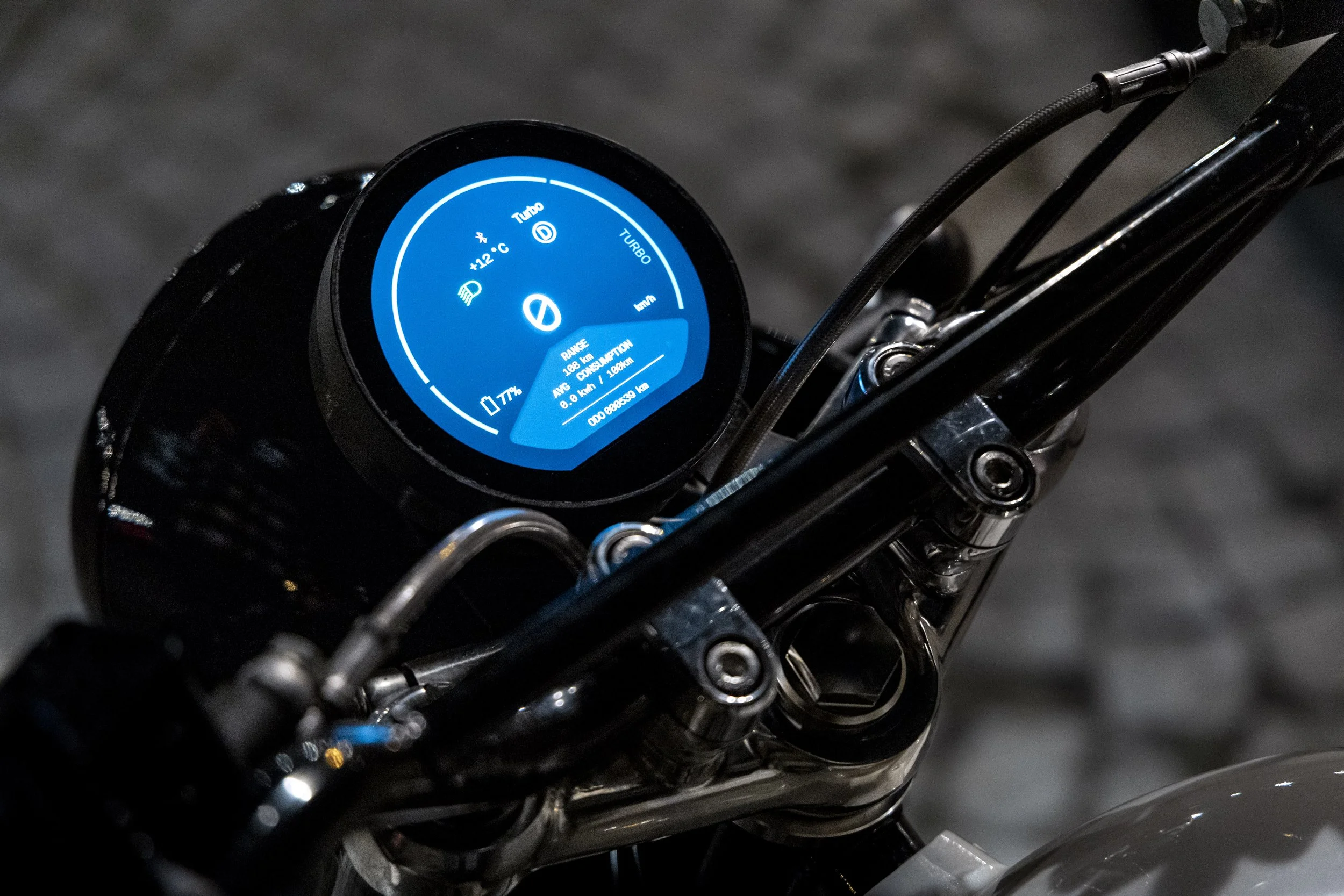 Tableau de bord numérique d'une moto électrique affichant des données de vitesse, de range, de température et d'autres informations en bleu sur un fond noir.