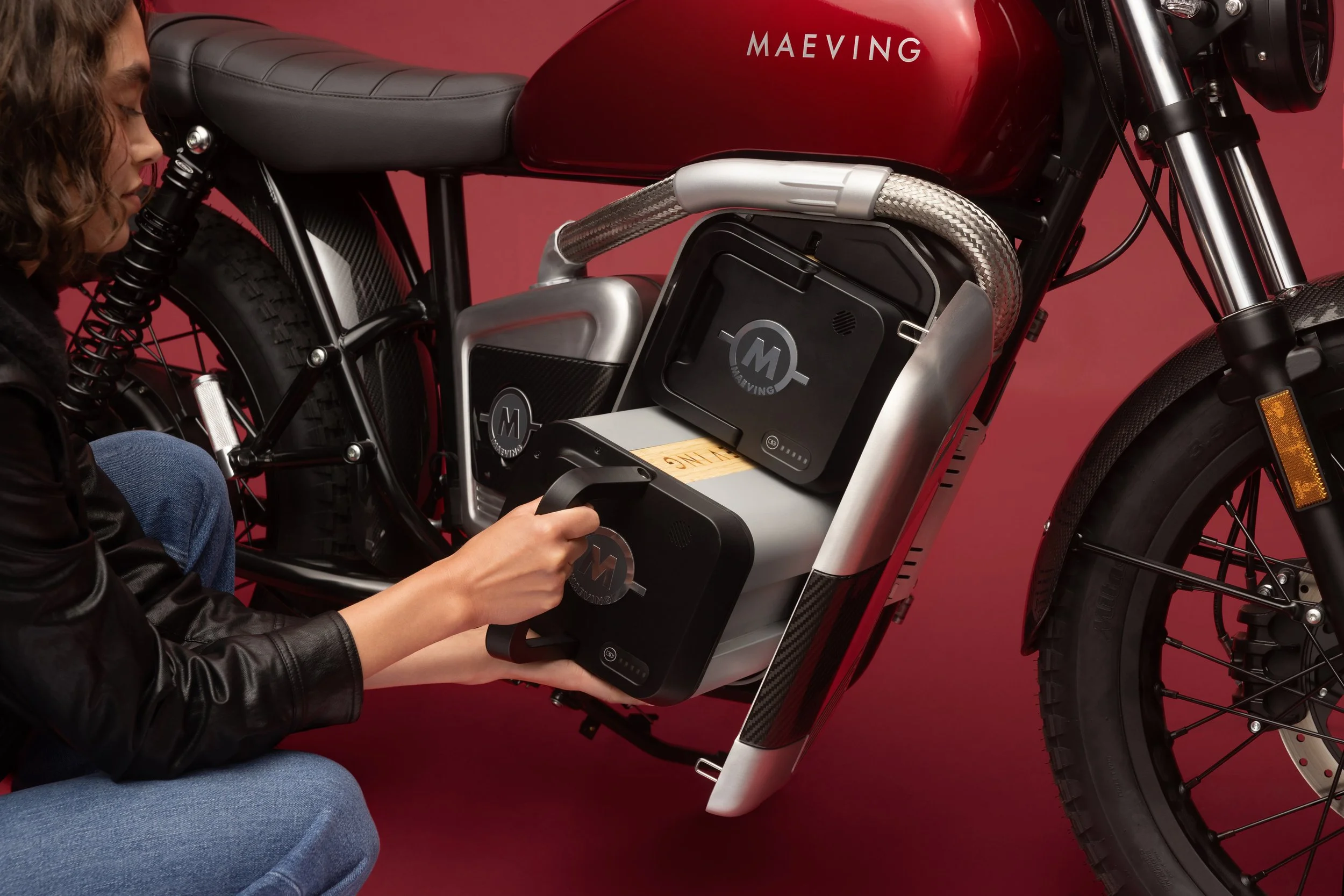 Femme s'appuyant sur une moto électrique de couleur rouge, avec un casque dans la main