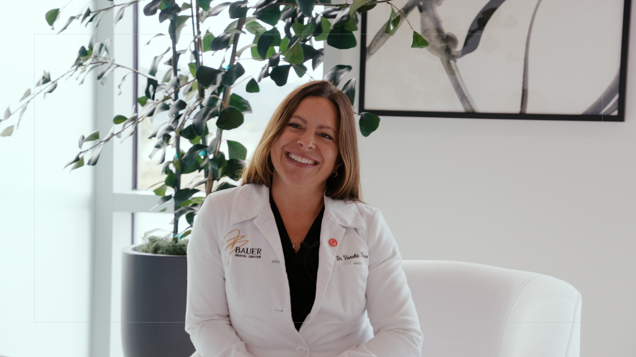 Smiling female dentist in a white lab coat seated in a modern dental office