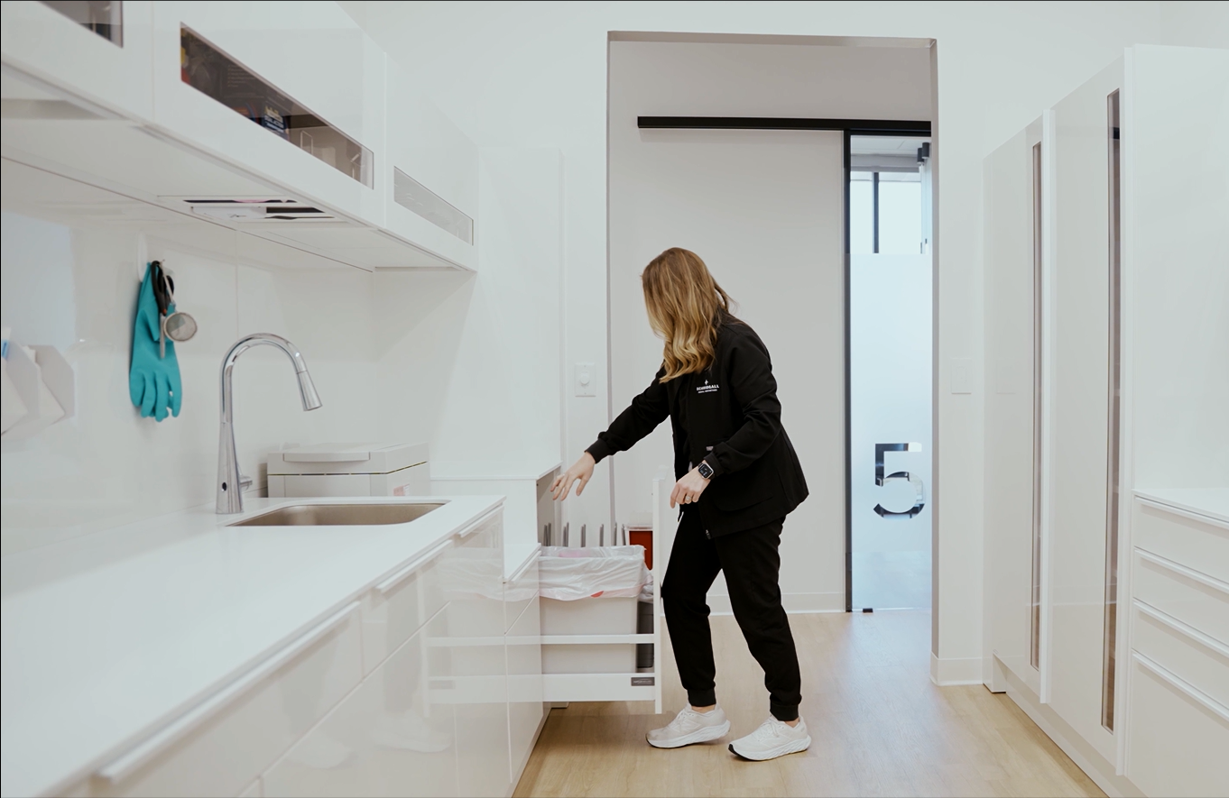 A woman in black uniform opening a drawer in a white, modern kitchen.