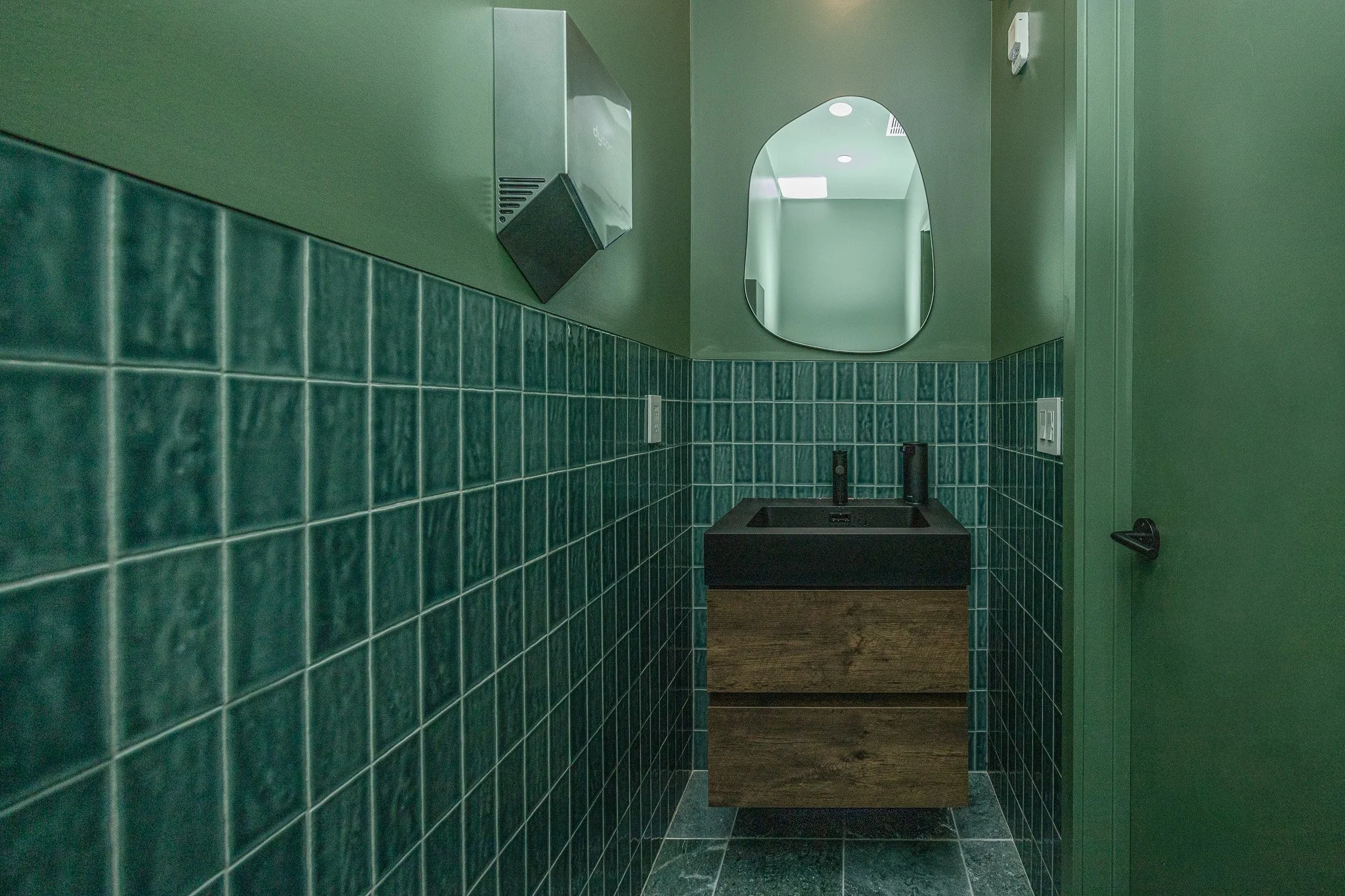 Green-tiled restroom at Polish Dental in NoHo, New York City, featuring contemporary fixtures, warm lighting, and hospitality-inspired healthcare design.