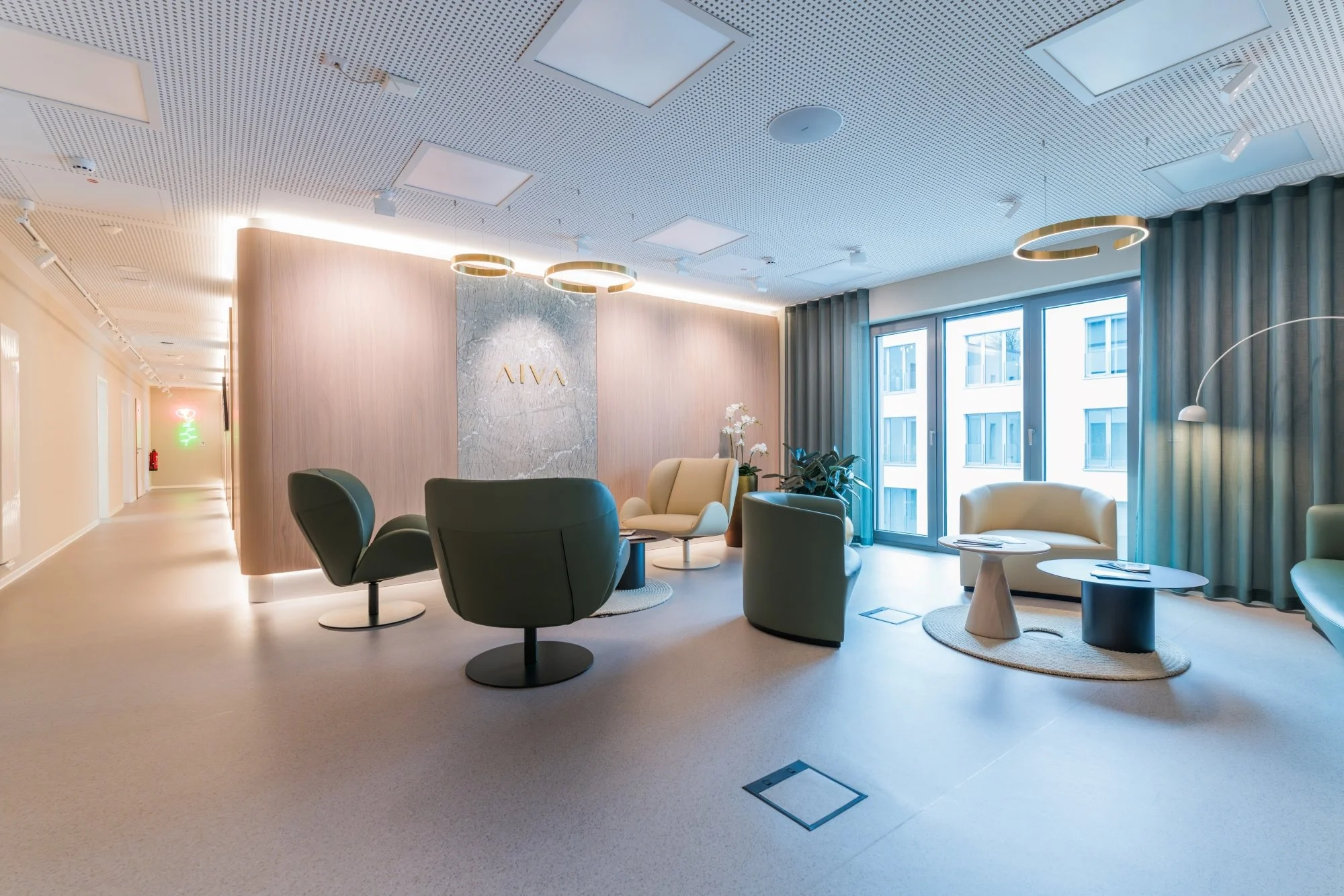 A modern, stylish waiting or lounge area with various chairs and small tables, large windows with blue curtains, and decorative lighting.