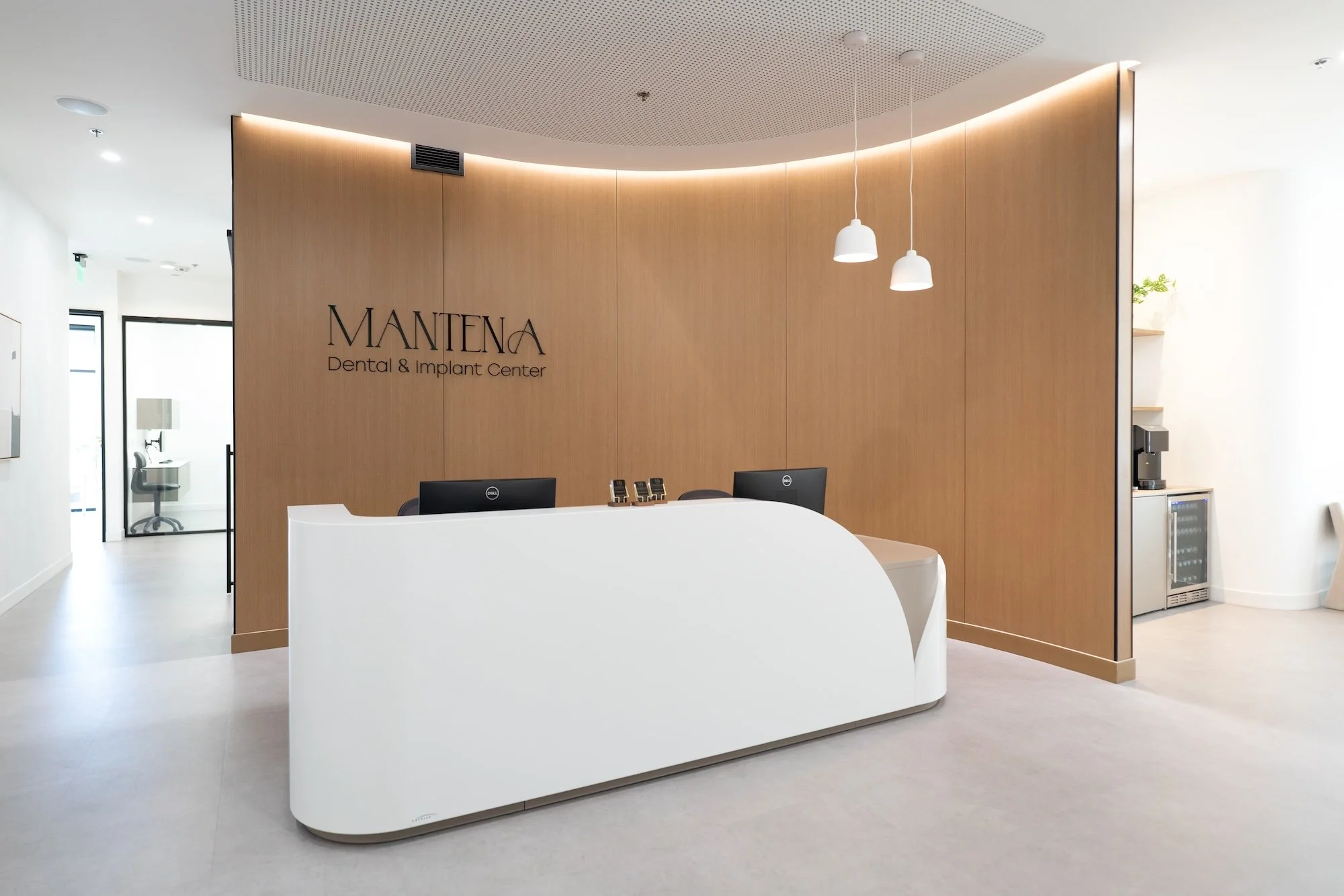 Reception area of a dental and implant center with a white curved desk, wooden wall with the center's name, and modern minimal decor.