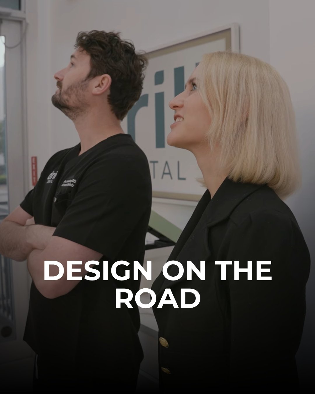 Two professionals standing side by side, one man with curly hair and a beard, and one woman with straight blonde hair, looking up with smiles. They are indoors near a sign that says 'aric' and 'TAL'. The text 'Design on the Road' is overlaid on the i
