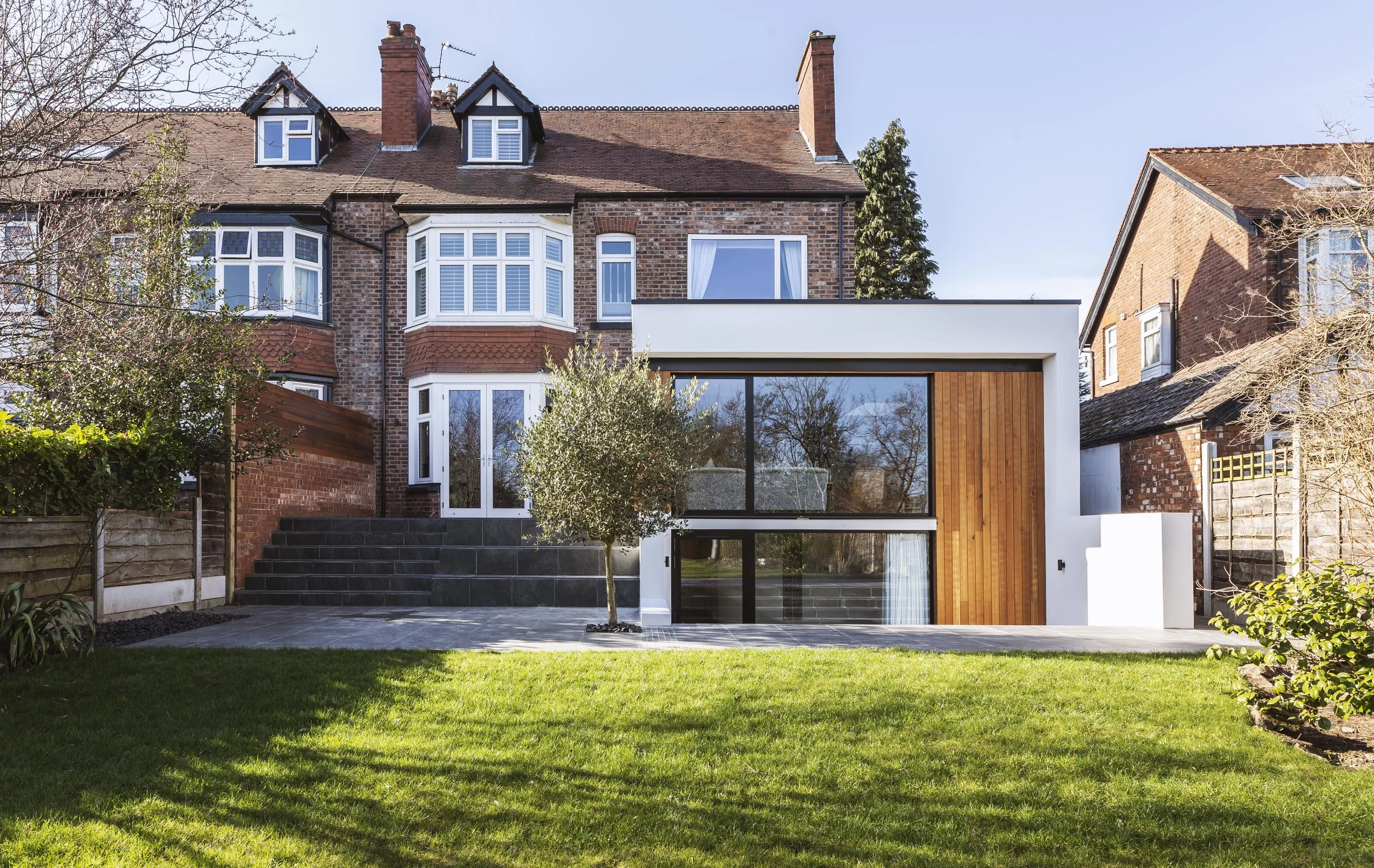 Guy Taylor Associates — South Manchester, Chorlton architect, Modern house with large glass windows, brick and wood exterior, and a backyard with grass, small tree, and patio