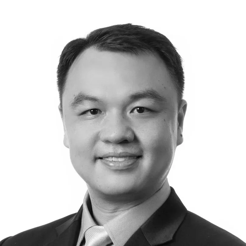 Black and white professional portrait of an Asian man in a suit and tie, smiling at the camera.