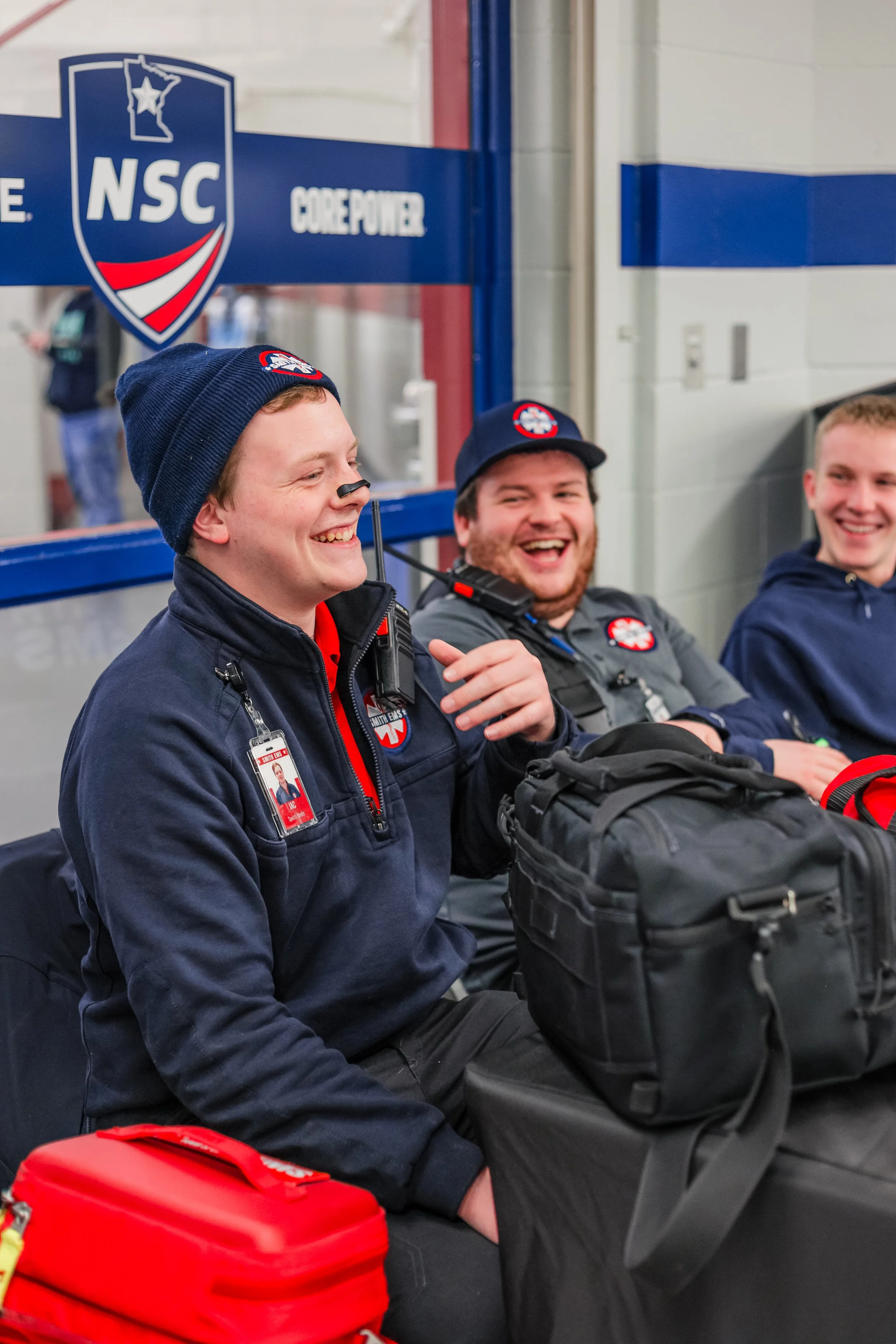 Three Smith EMS medics in uniform sitting and smiling at a hockey tournament.